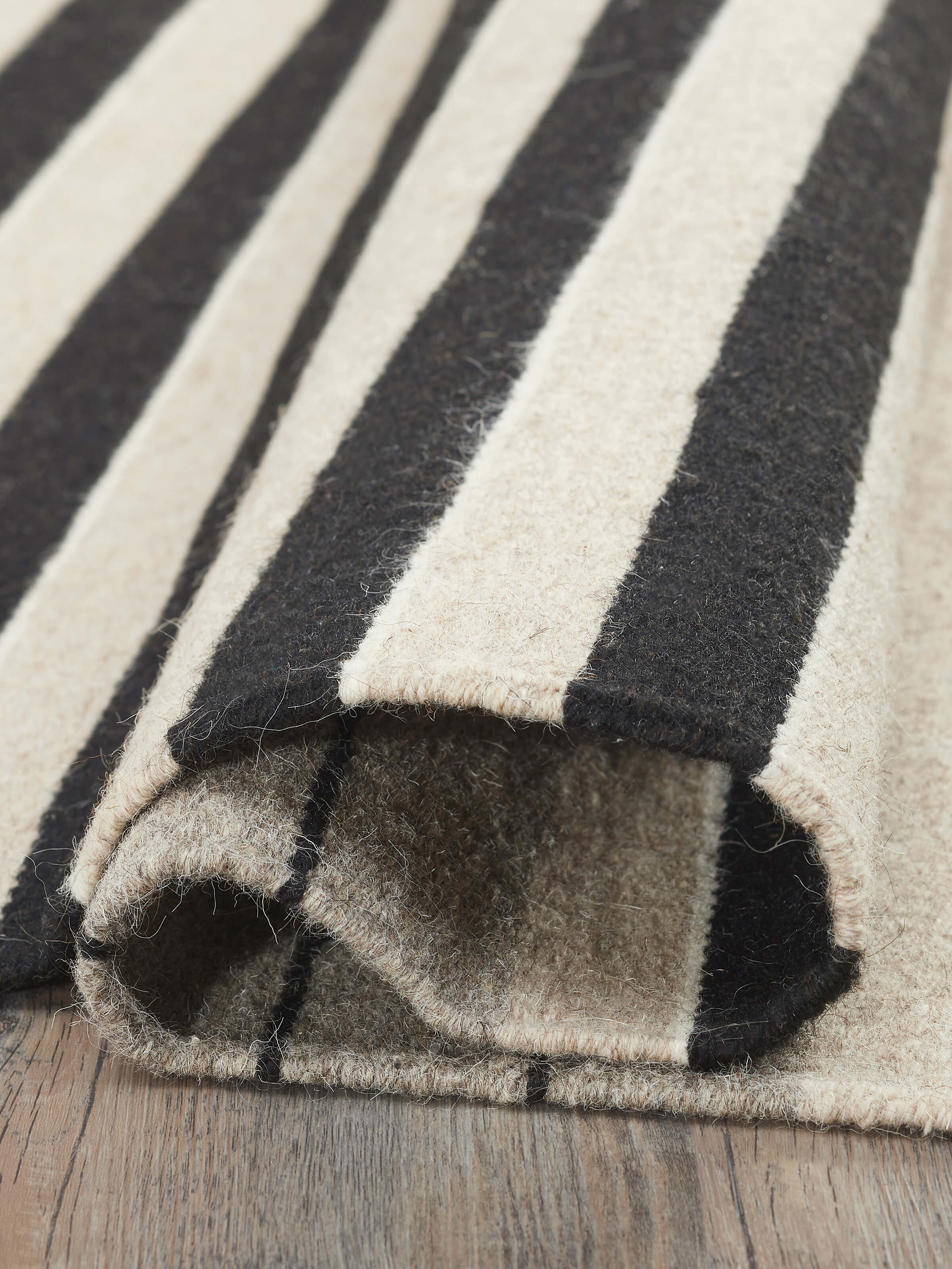 Side view of Nomad Stripes Black Beige Jawaja Wool & Cotton Handloom Dhurrie (3x5 ft) emphasizing its durability and handloom craftsmanship