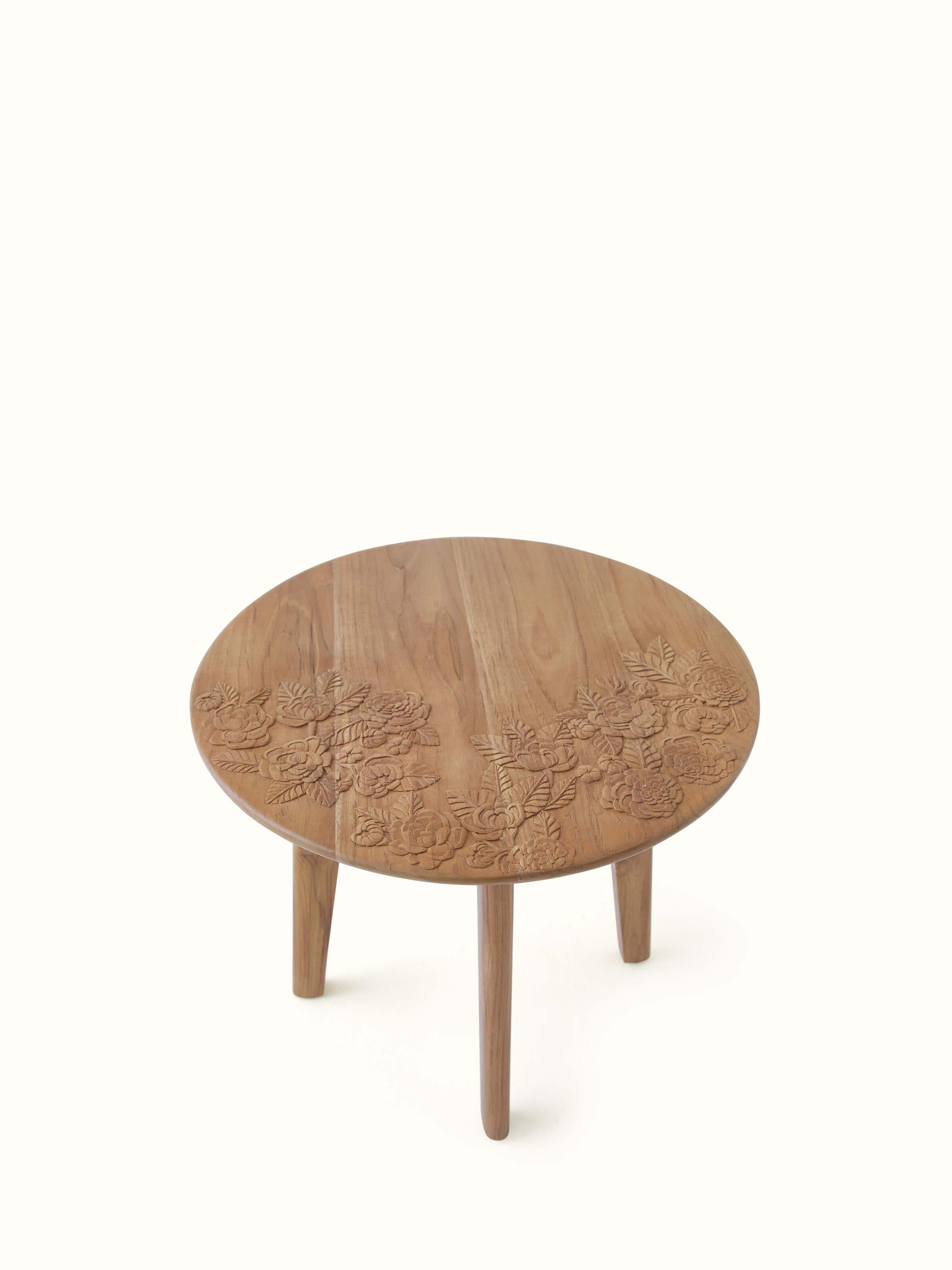 Angled view of the teak wood side table, emphasizing the detailed carvings and round tabletop