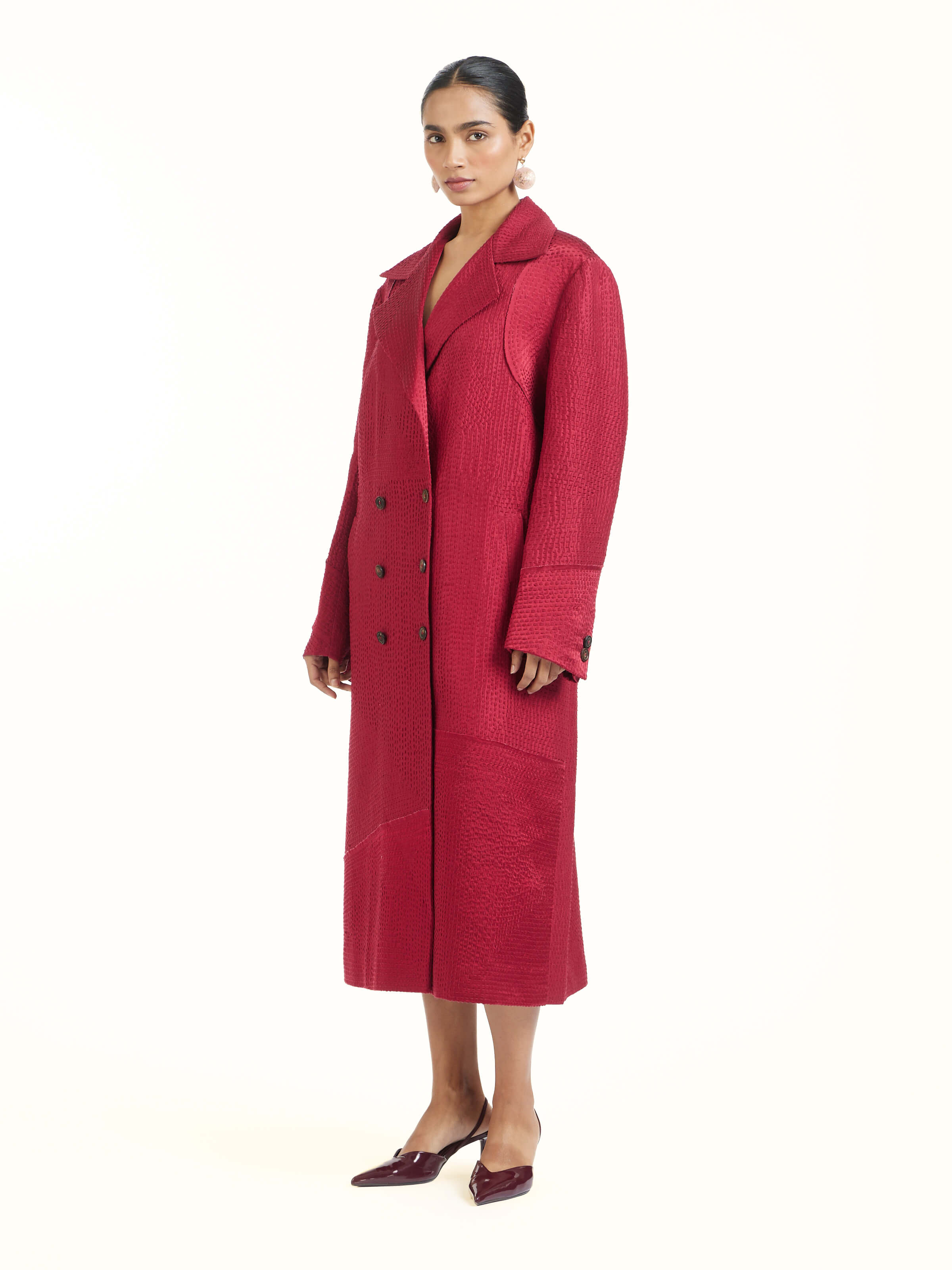 Side view of red silk kantha trench coat highlighting structured silhouette and fall