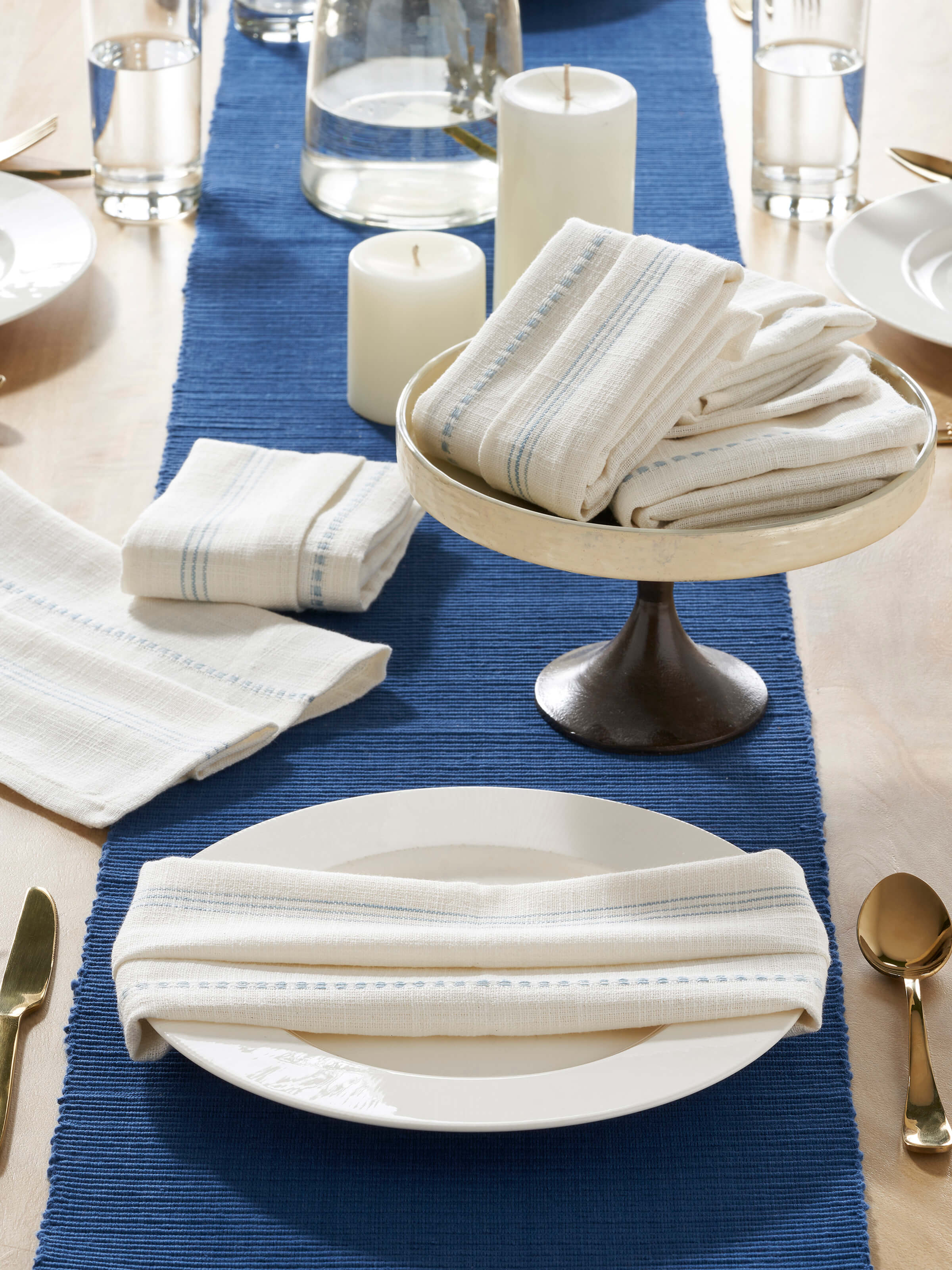Lifestyle view of Arth light blue stripe cotton handloom dinner napkins arranged on a wooden dining table with tableware.