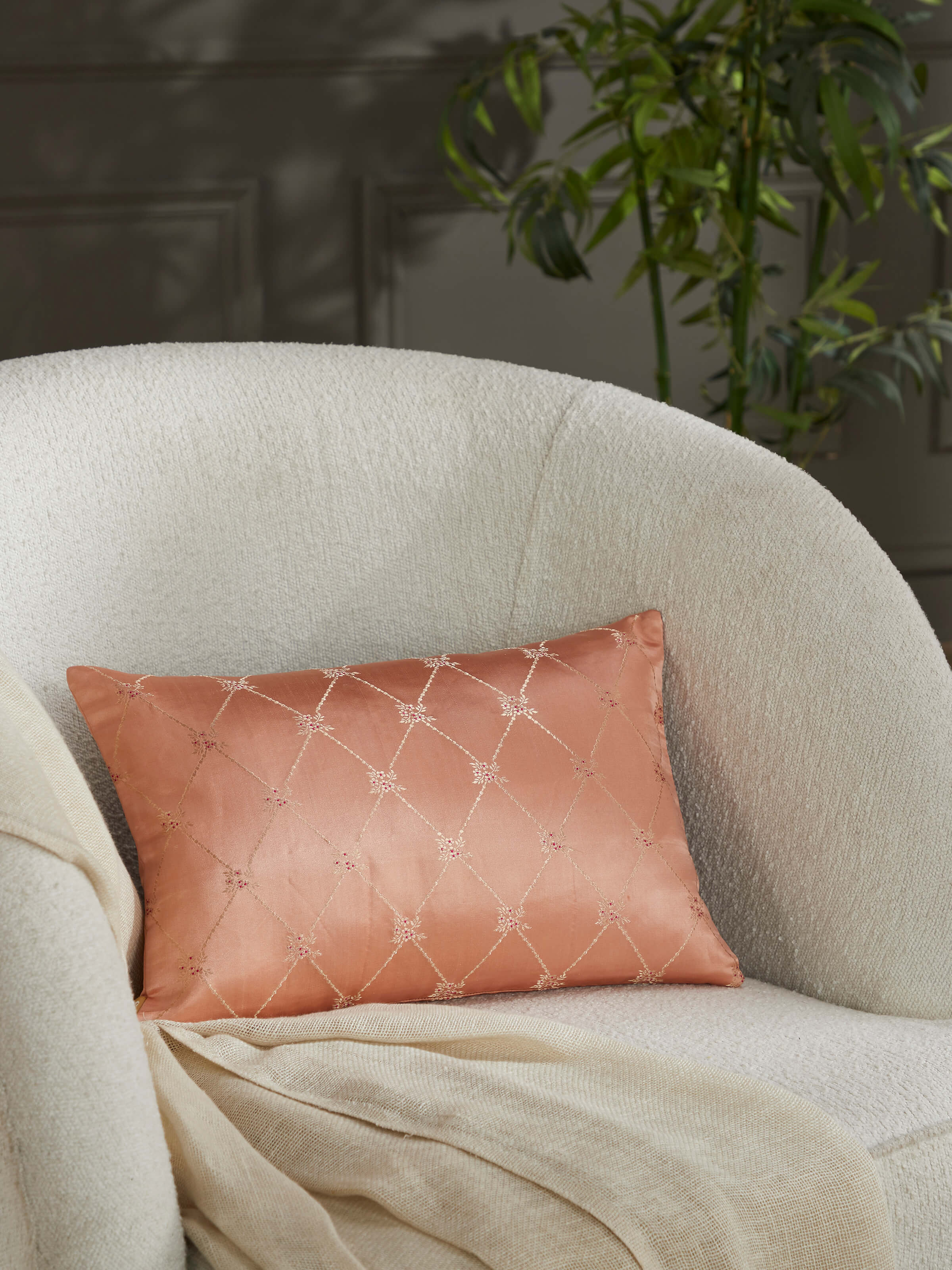 Lifestyle view of Awadh peach handloom silk cushion cover placed on a sofa.