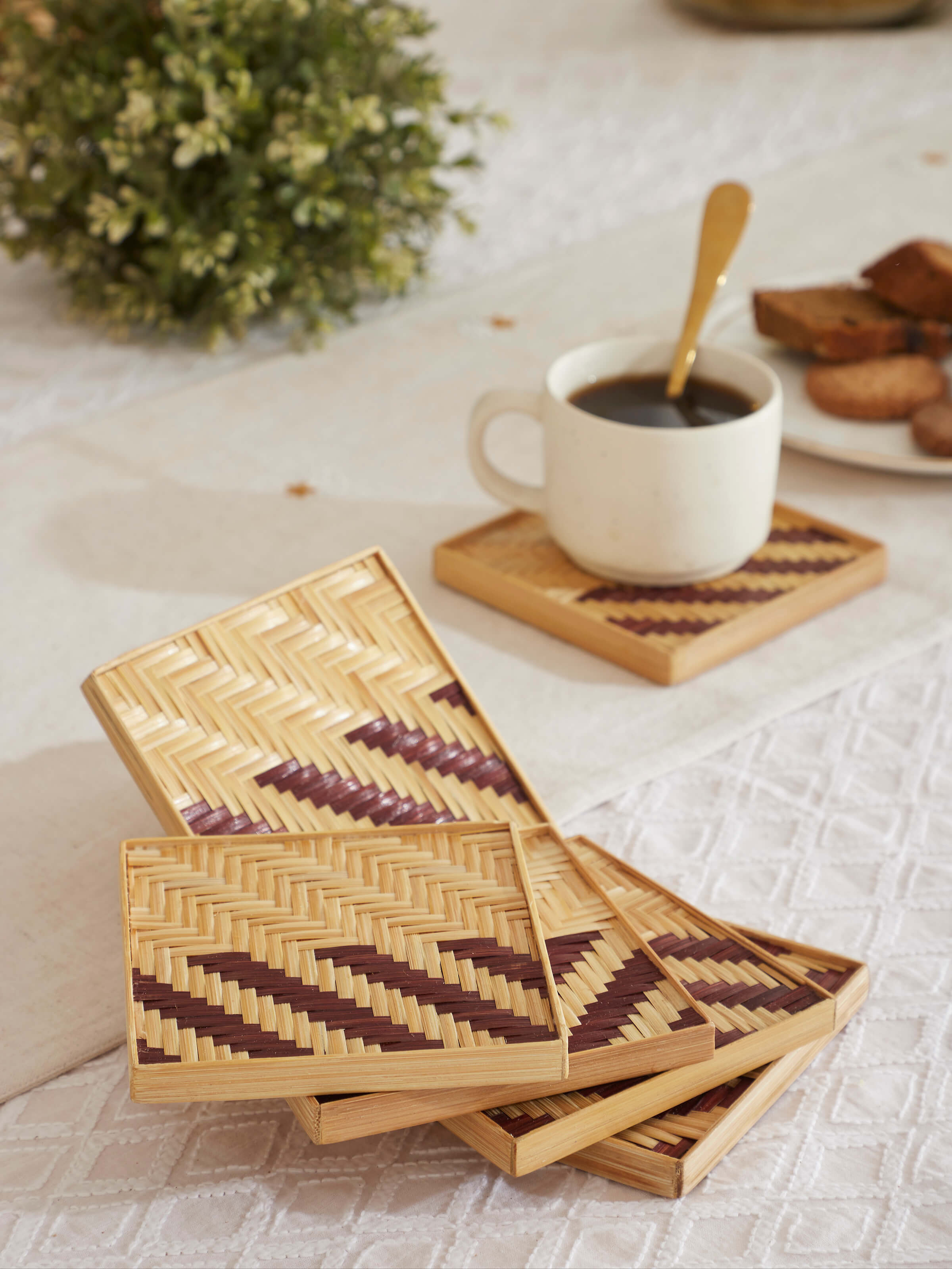 Lifestyle view of Naveena brown bamboo coasters placed under mugs on a wooden table in a cozy dining setting.