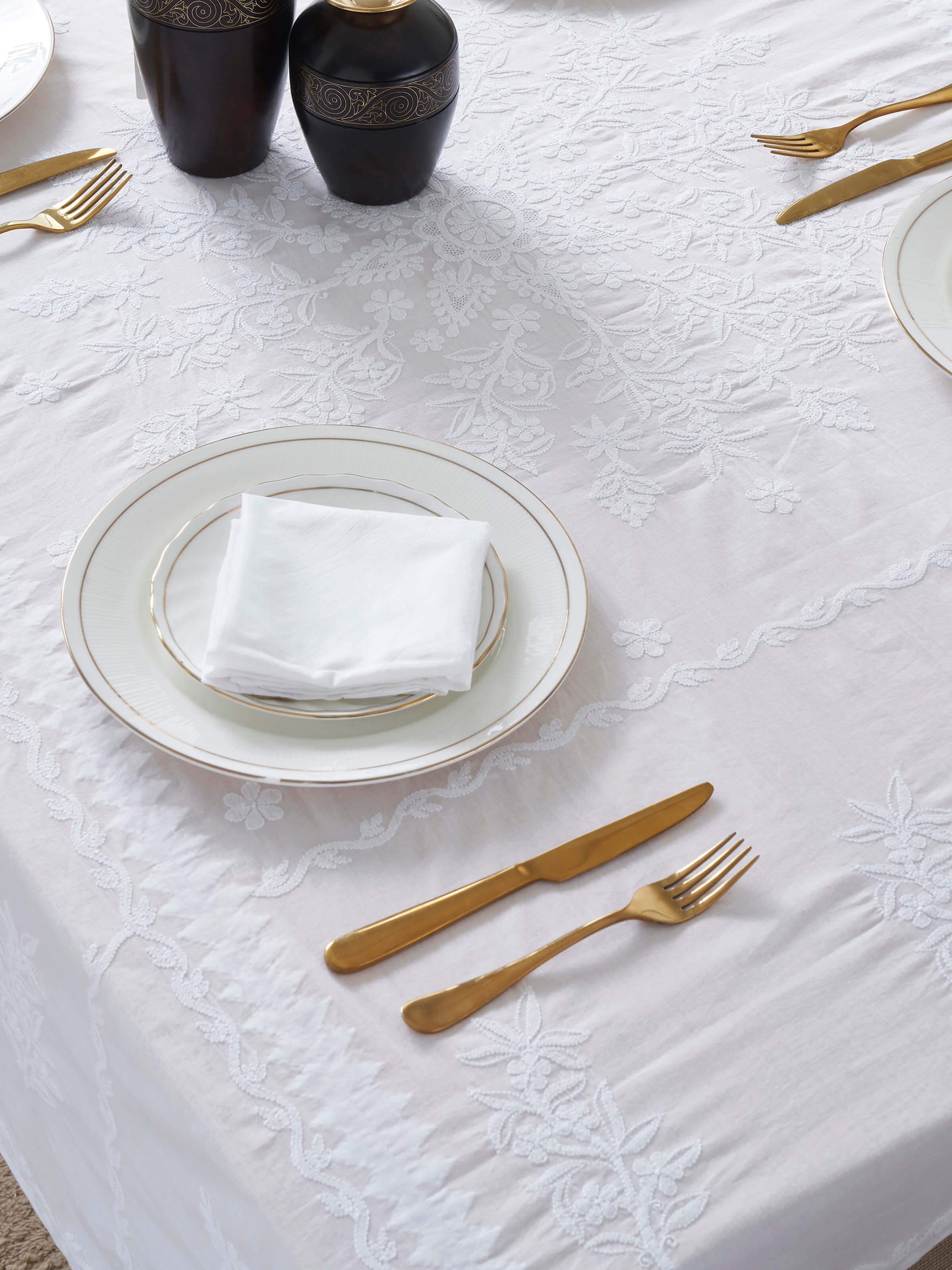 Lifestyle view of Ananda white cotton Chikankari table cover styled with ceramic serveware and fresh flowers.