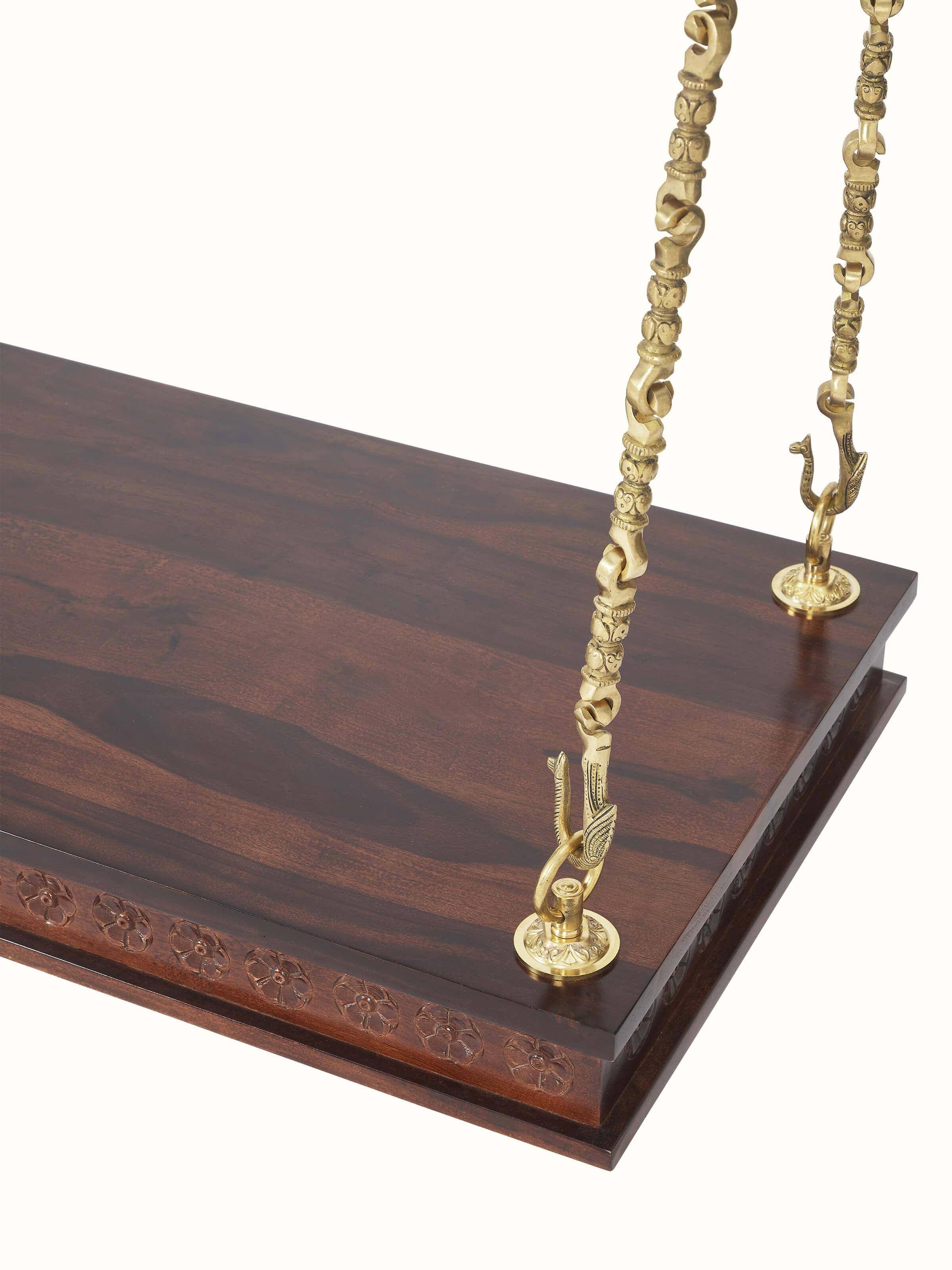 Angled view of the carved Sheesham wood swing with brass accents, highlighting the swing's elegant structure and design.