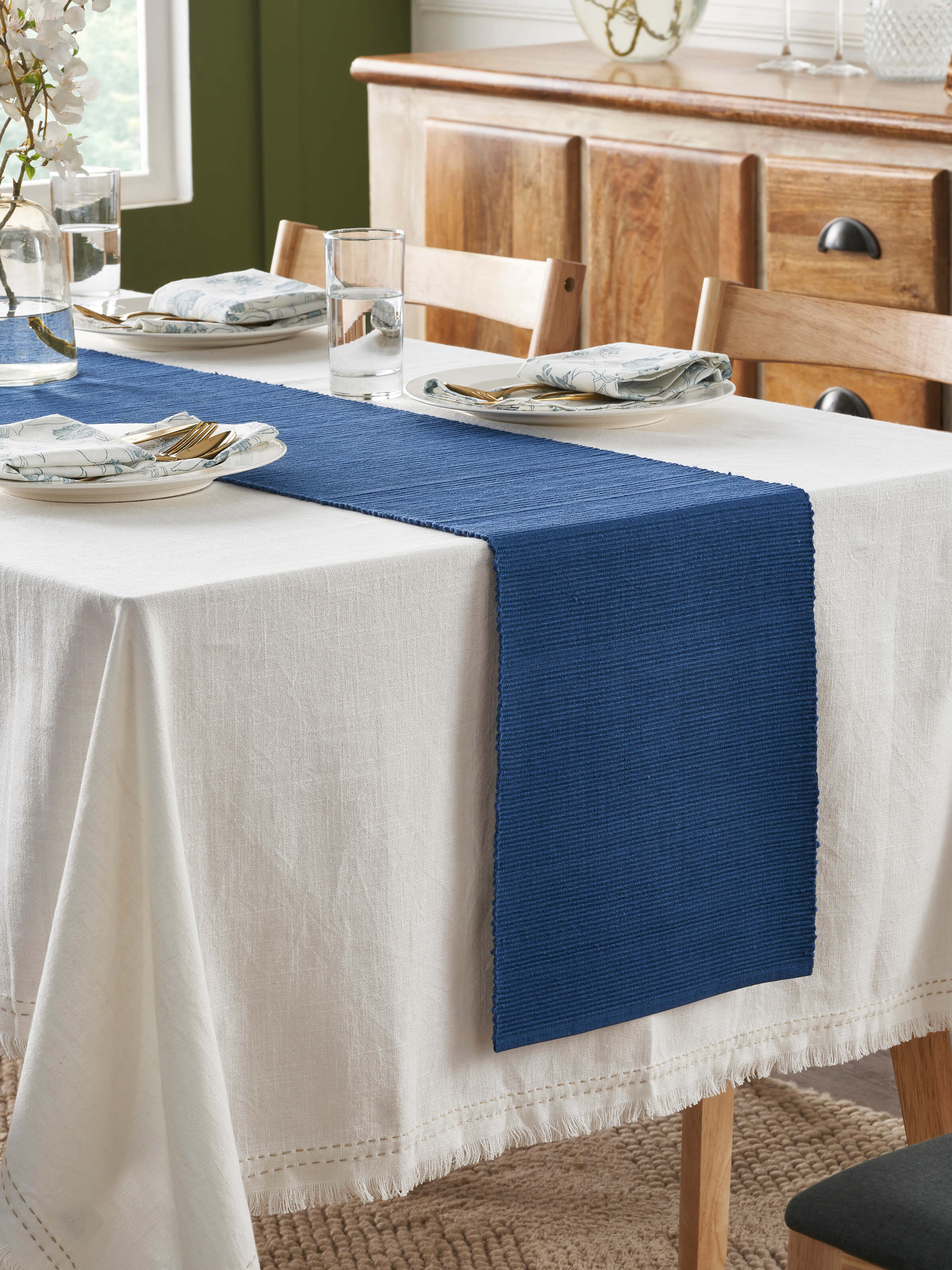Lifestyle view of Vastav indigo cotton handloom table runner styled with plates and cutlery on a dining table.