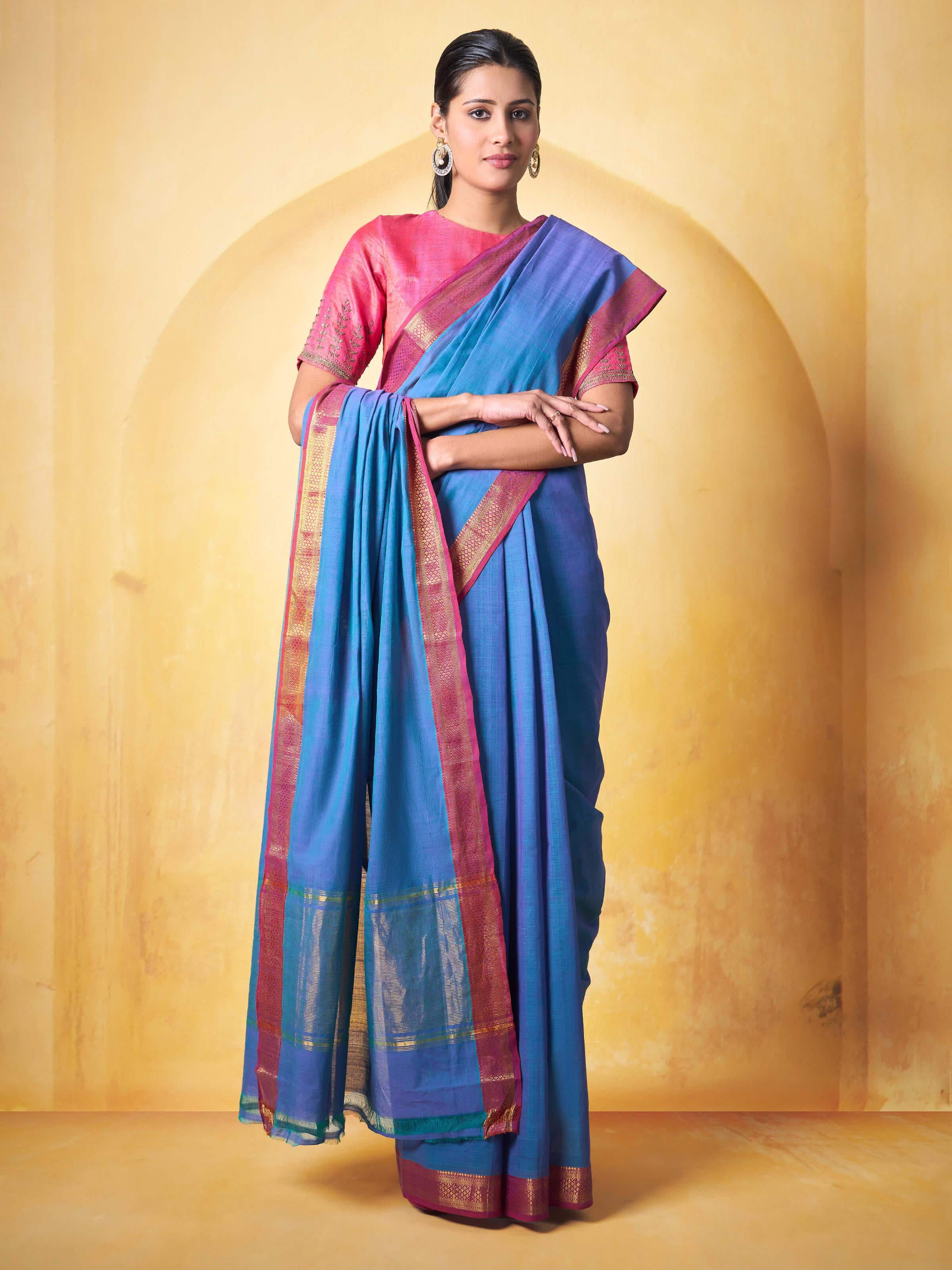 Woman wearing blue and pink Mangalgiri cotton saree, styled traditionally in a home setting.