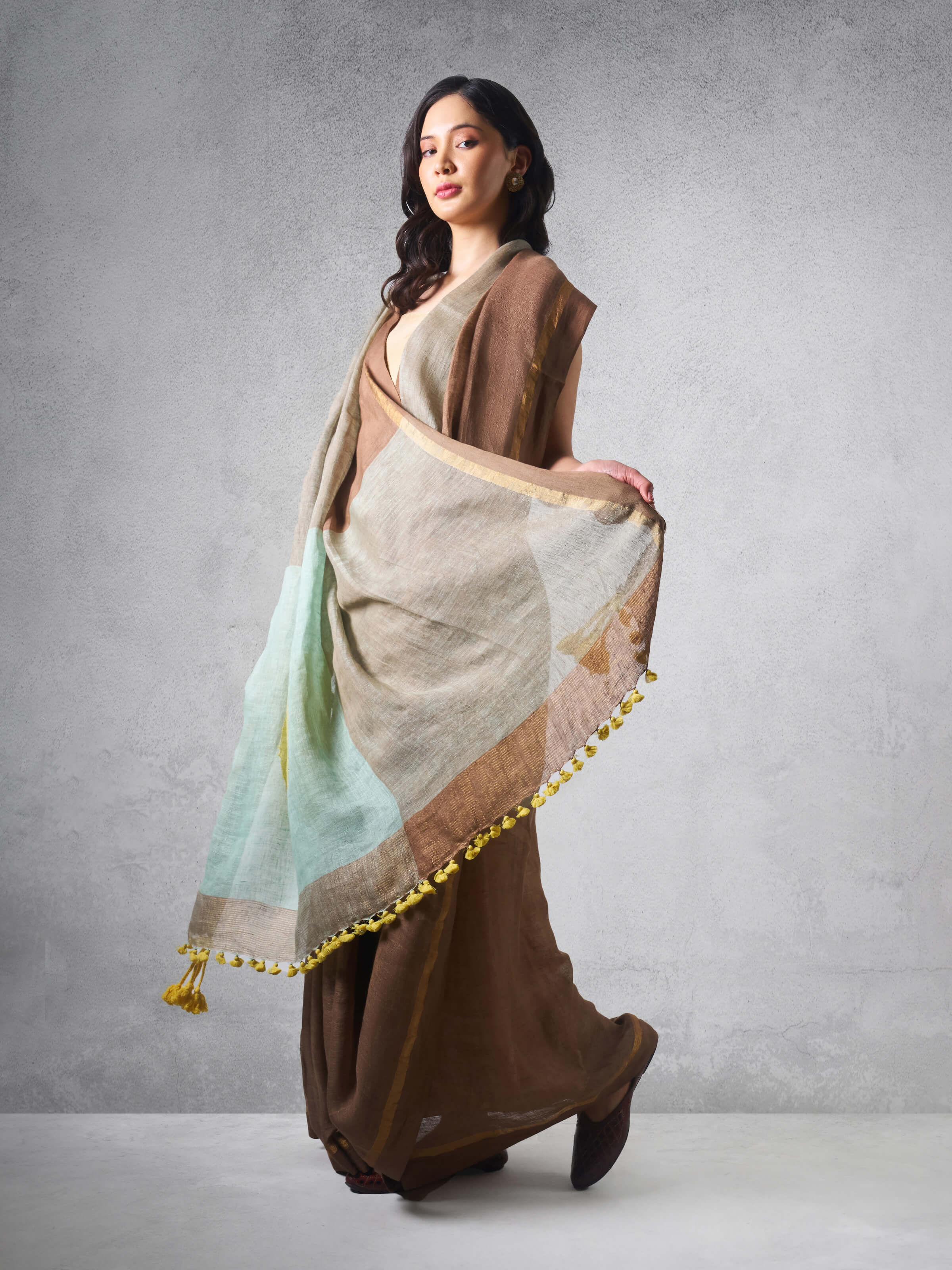 Lifestyle shot of beige linen cotton saree worn traditionally with pleats.