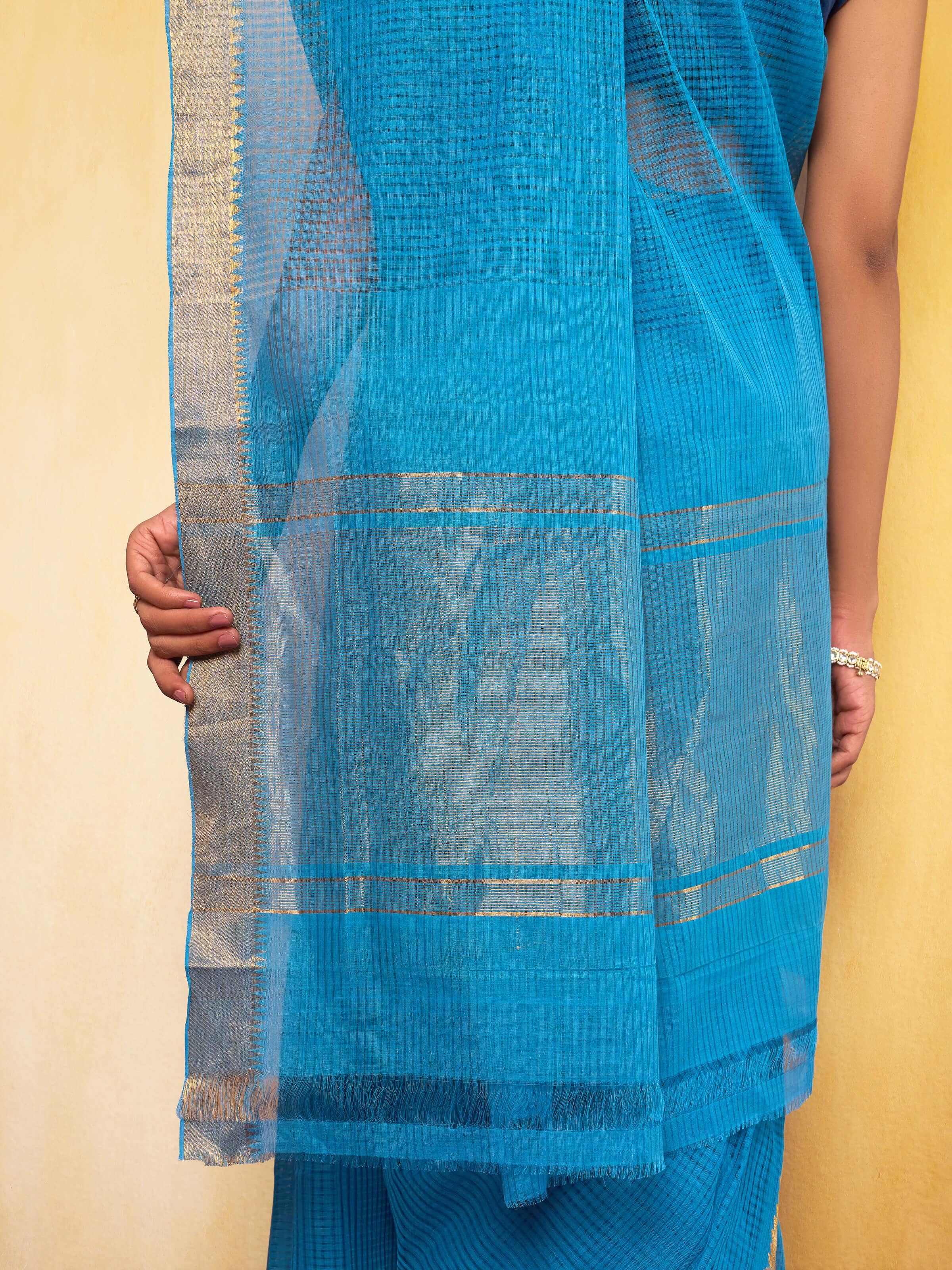Detailed view of the saree drape displaying its fine cotton texture and gold zari detailing.