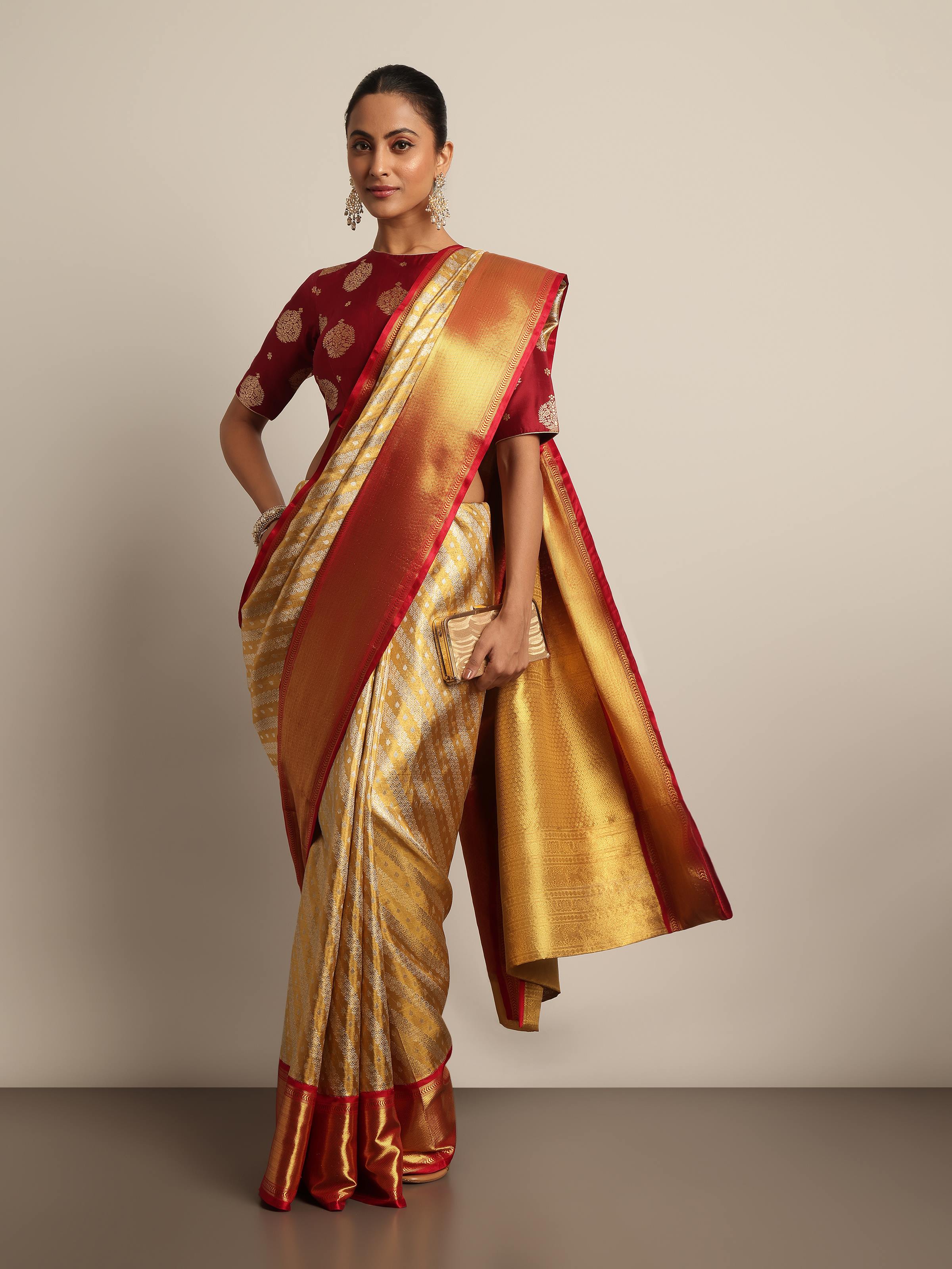 Elegant pose in gold Kancheepuram saree with ornate temple backdrop.