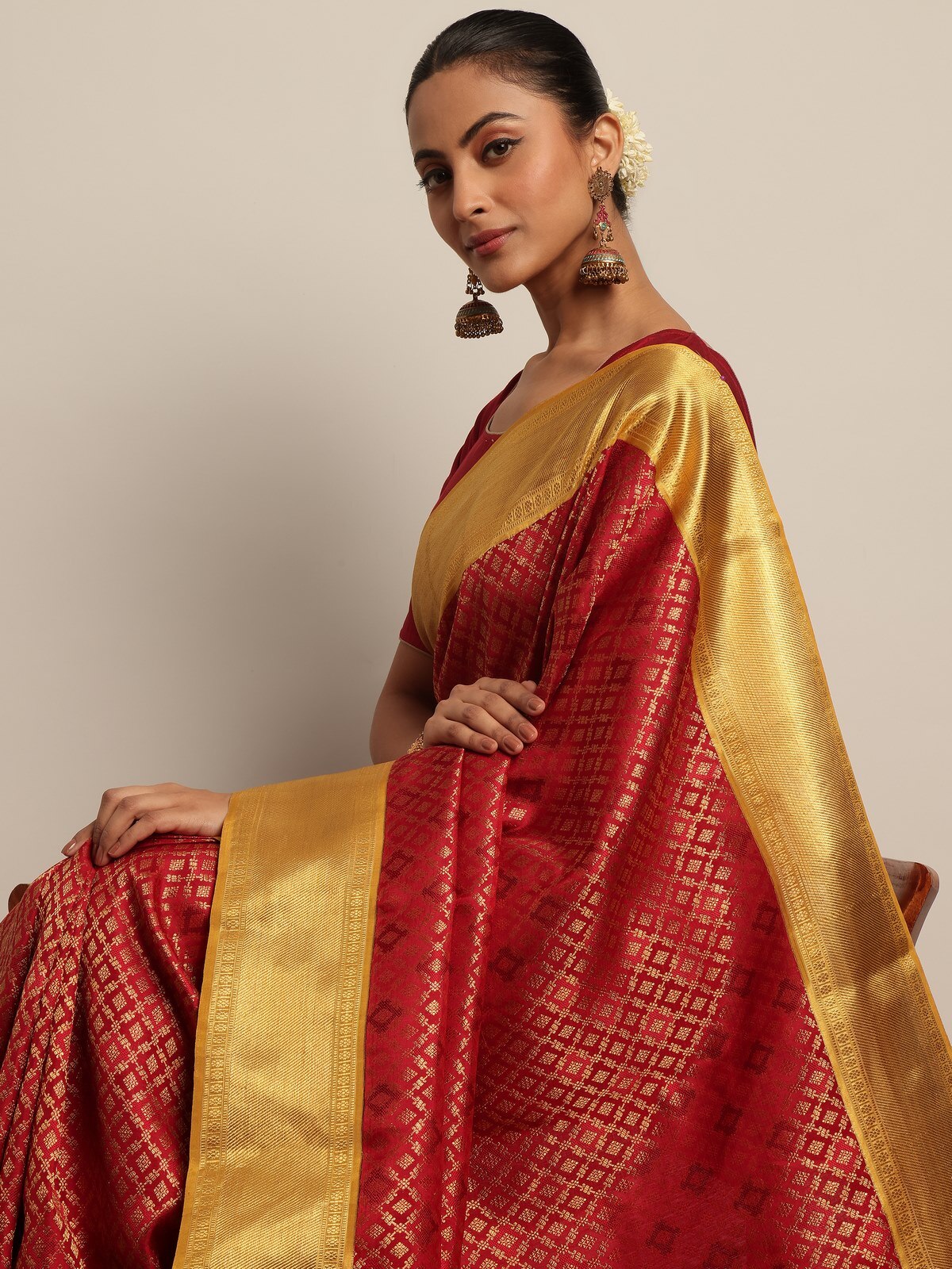 Side angled view of model wearing red silk Kancheepuram saree, emphasizing the grandeur of the woven motifs.