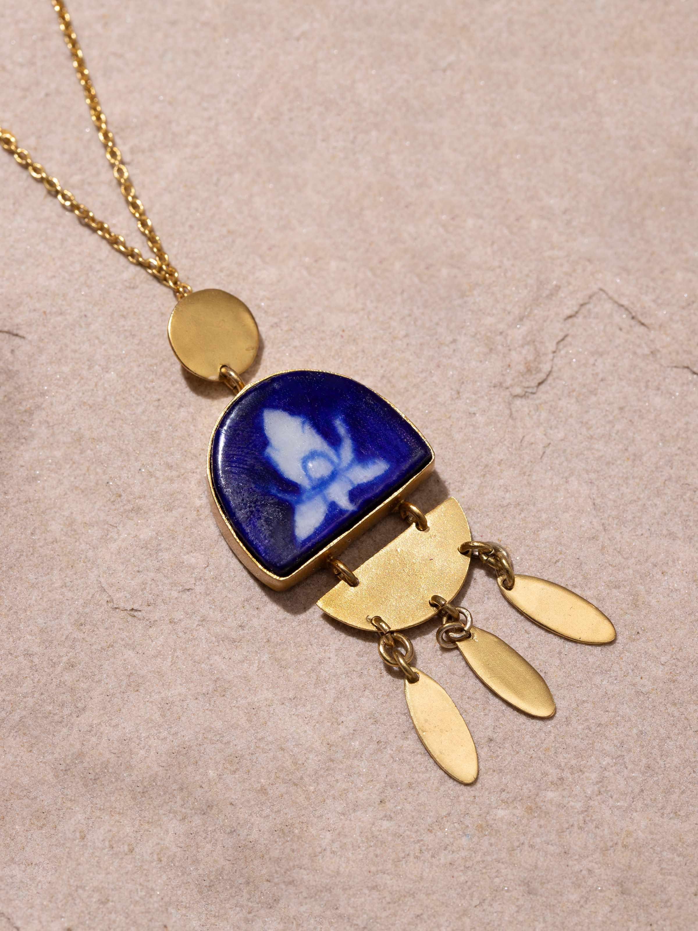 Blue pottery pendant and chain displayed on a flat surface, emphasizing its detailed design.
