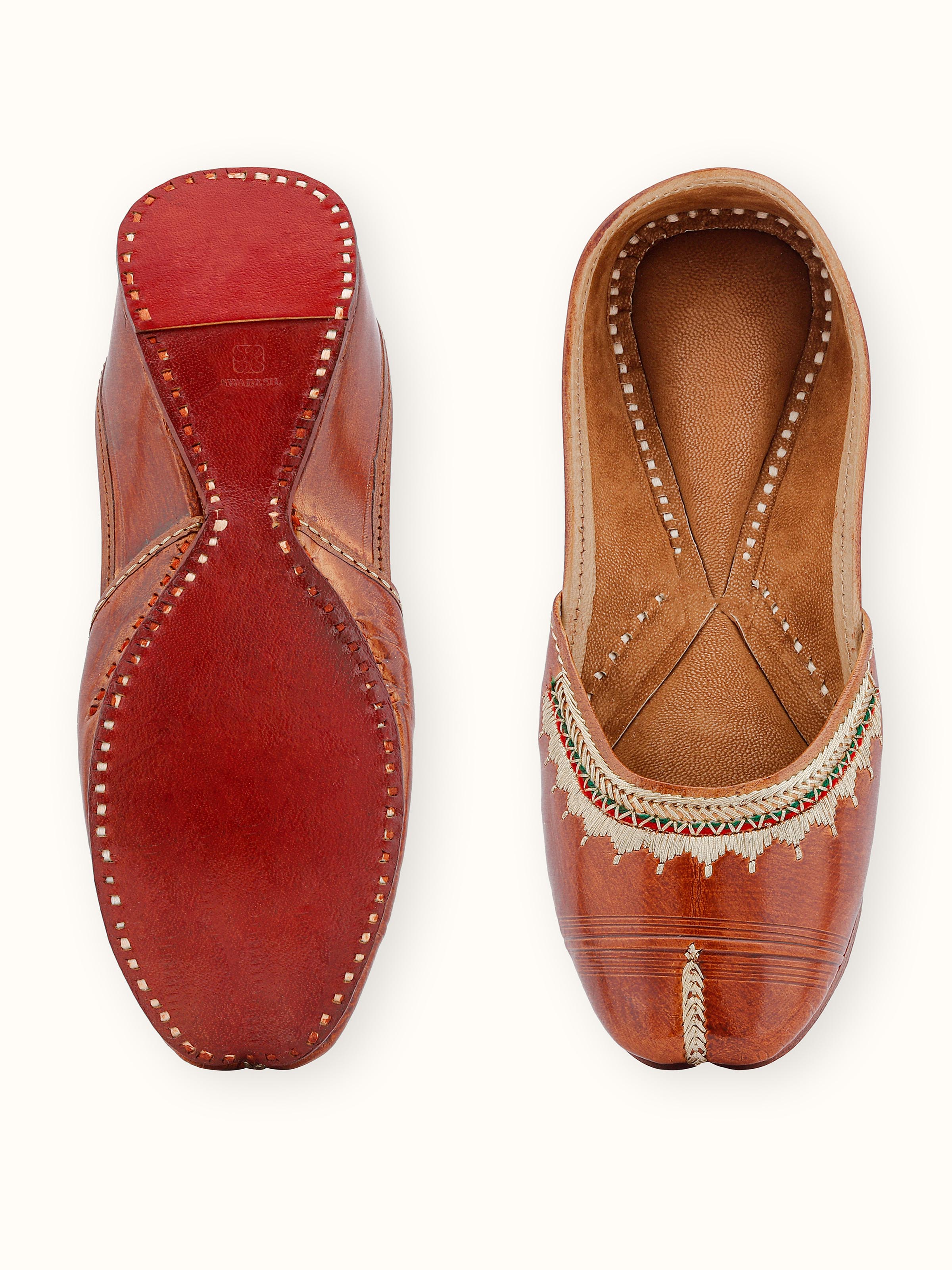 Detailed view of tan leather haryana juttis with focus on the stitching and design