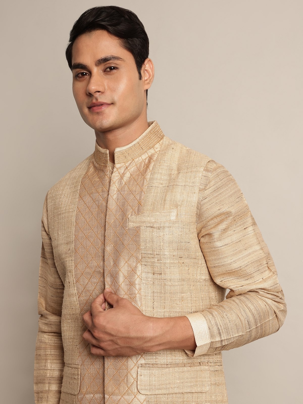 Angled view of sleeveless beige Tussar silk jacket showing neckline and hem finish.