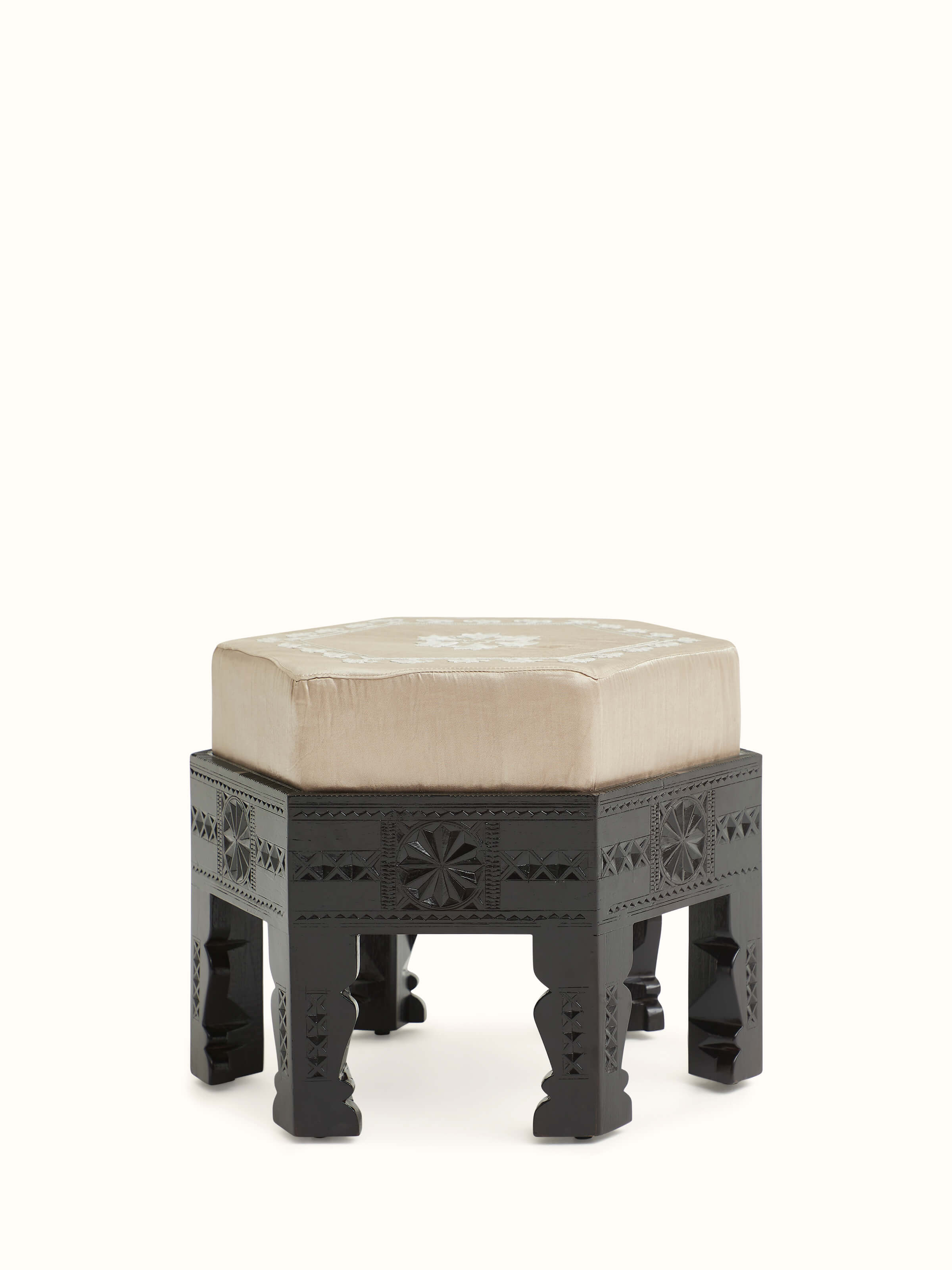 Angled view of upholstered carved teak wood round pouffe showing detailed carving work