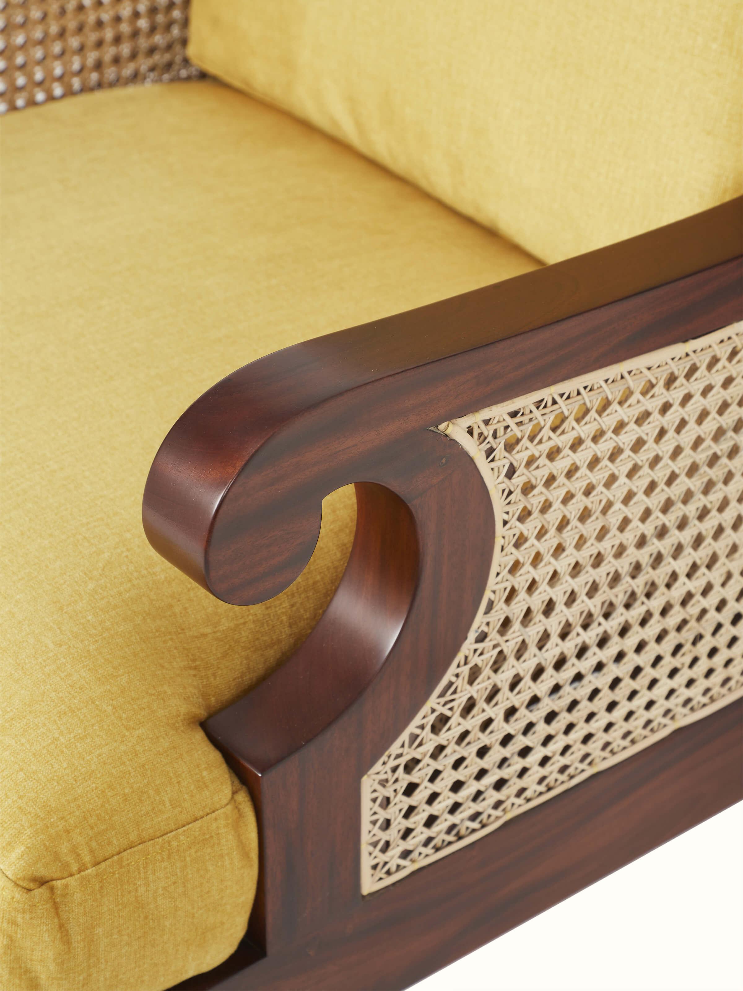 Close-up of upholstered mahogany wood & cane armchair, displaying intricate cane weaving and upholstery