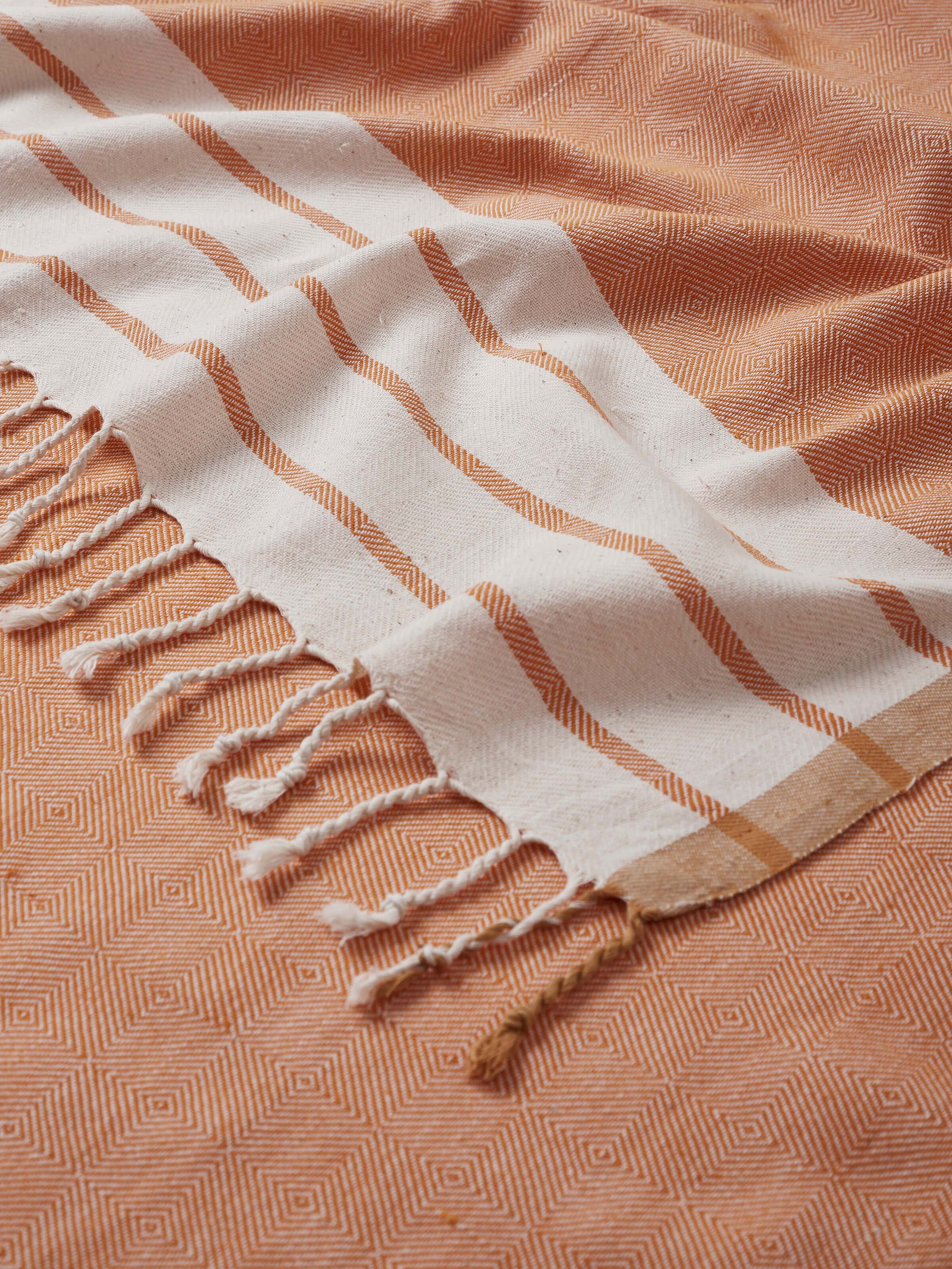 Side view of Samitha brown stripe cotton bath towel (L) illustrating its thickness and edge finish