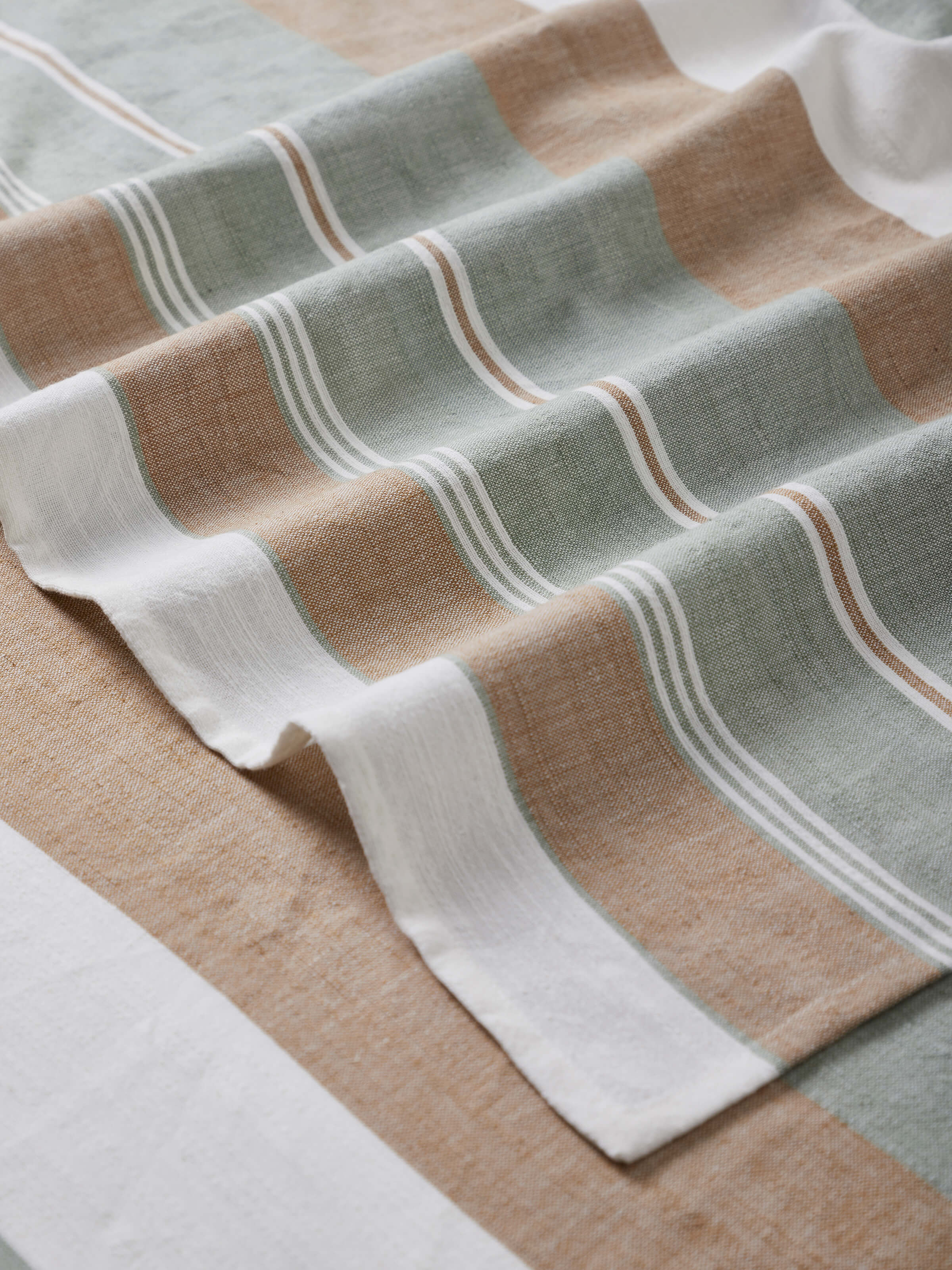 Detailed view of the edges and stitching on a green cotton striped bath towel, showcasing the durable construction.