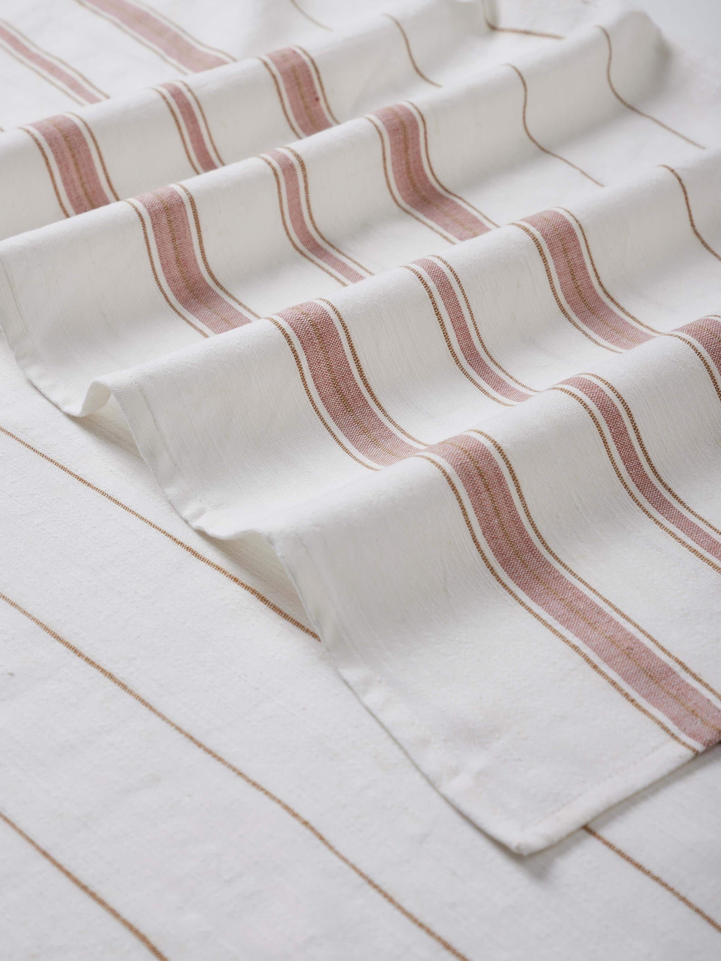 Adrita white cotton striped bath towel (L) displayed in a bathroom setting, emphasizing its size and elegant design.
