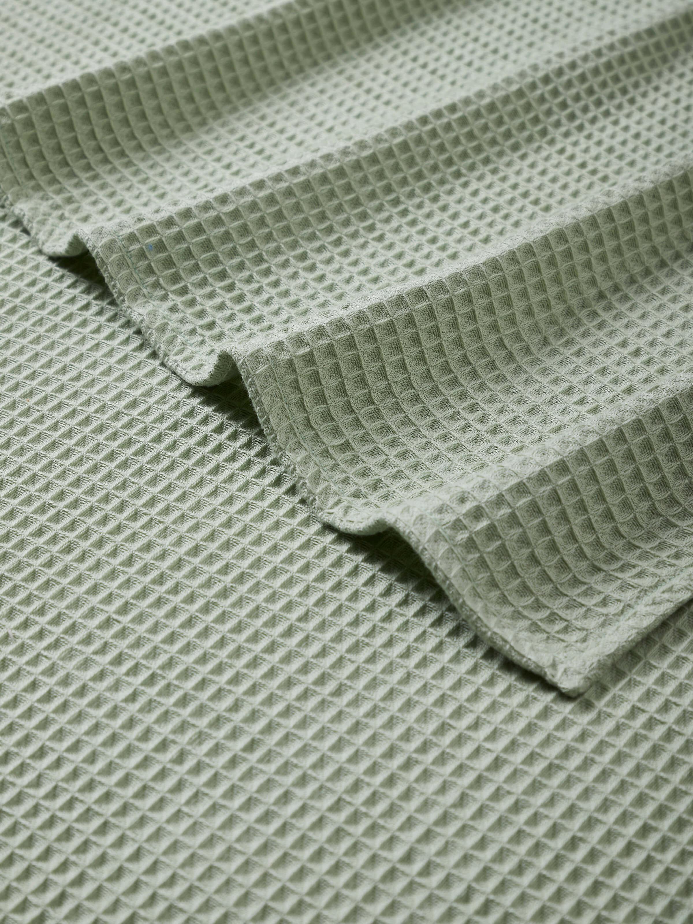Side view of Amala waffle green solid cotton bath towel showing its thickness and green color in natural light