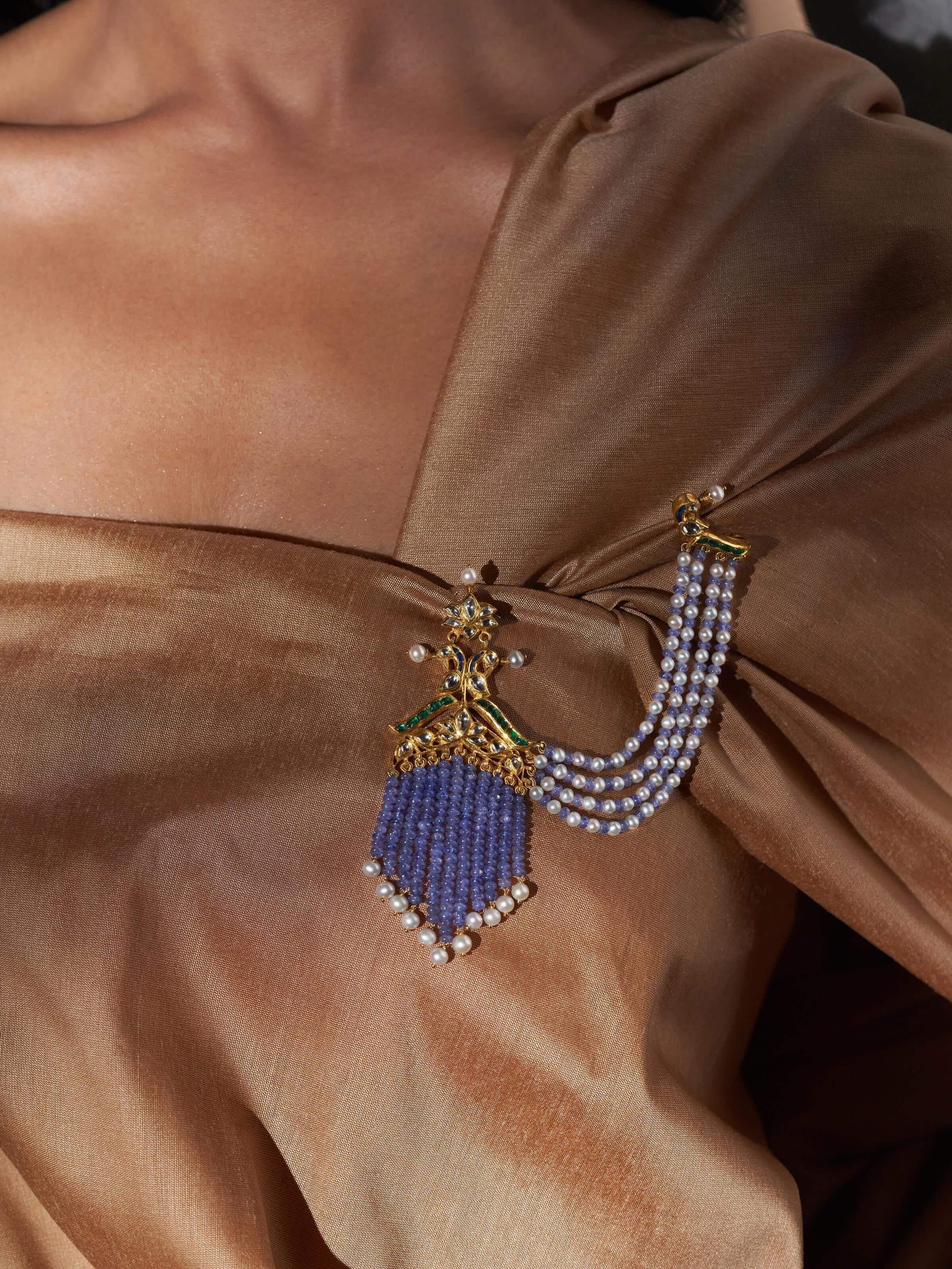 Lifestyle shot of Jadau 18 Karat gold brooch showcasing intricate stone setting and gold frame.