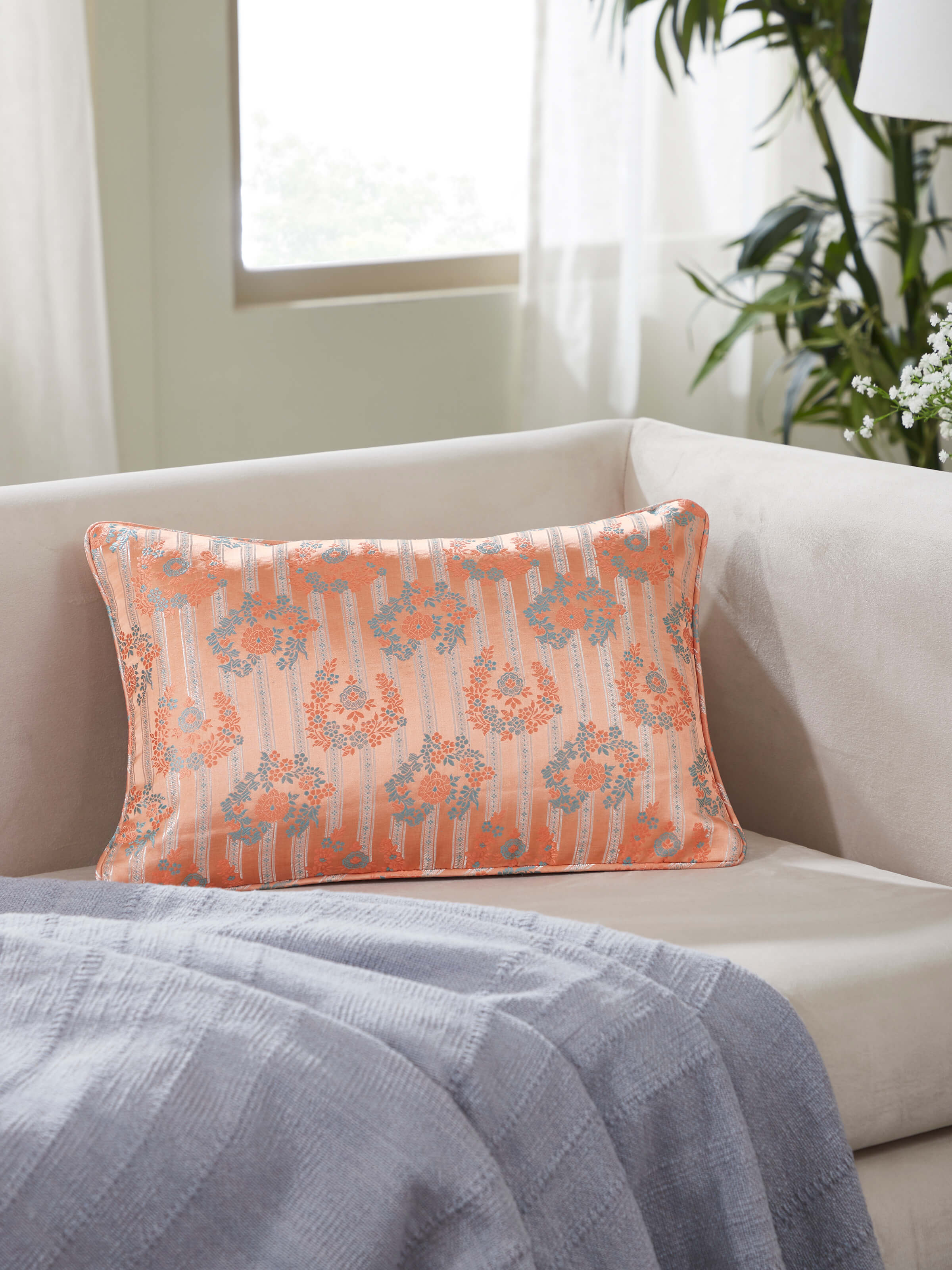 Lifestyle view of Banarasi silk cushion cover styled on a bench with peach and gold accents