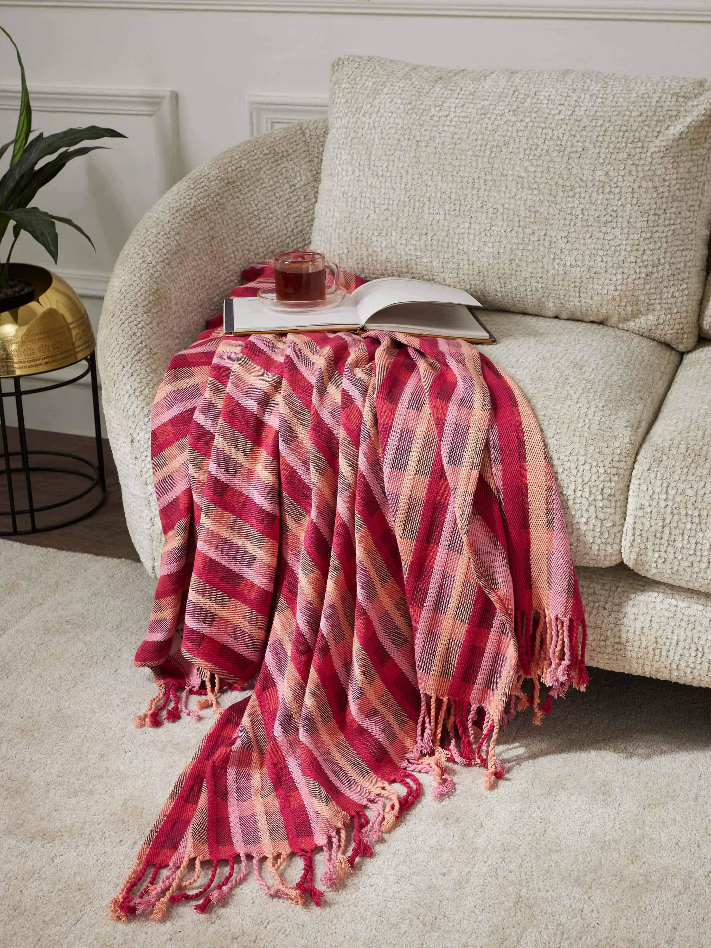 Lifestyle view of Niketa Raspberry Plaid Throw on a sofa, adding warmth and a touch of color to a neutral living room setup.