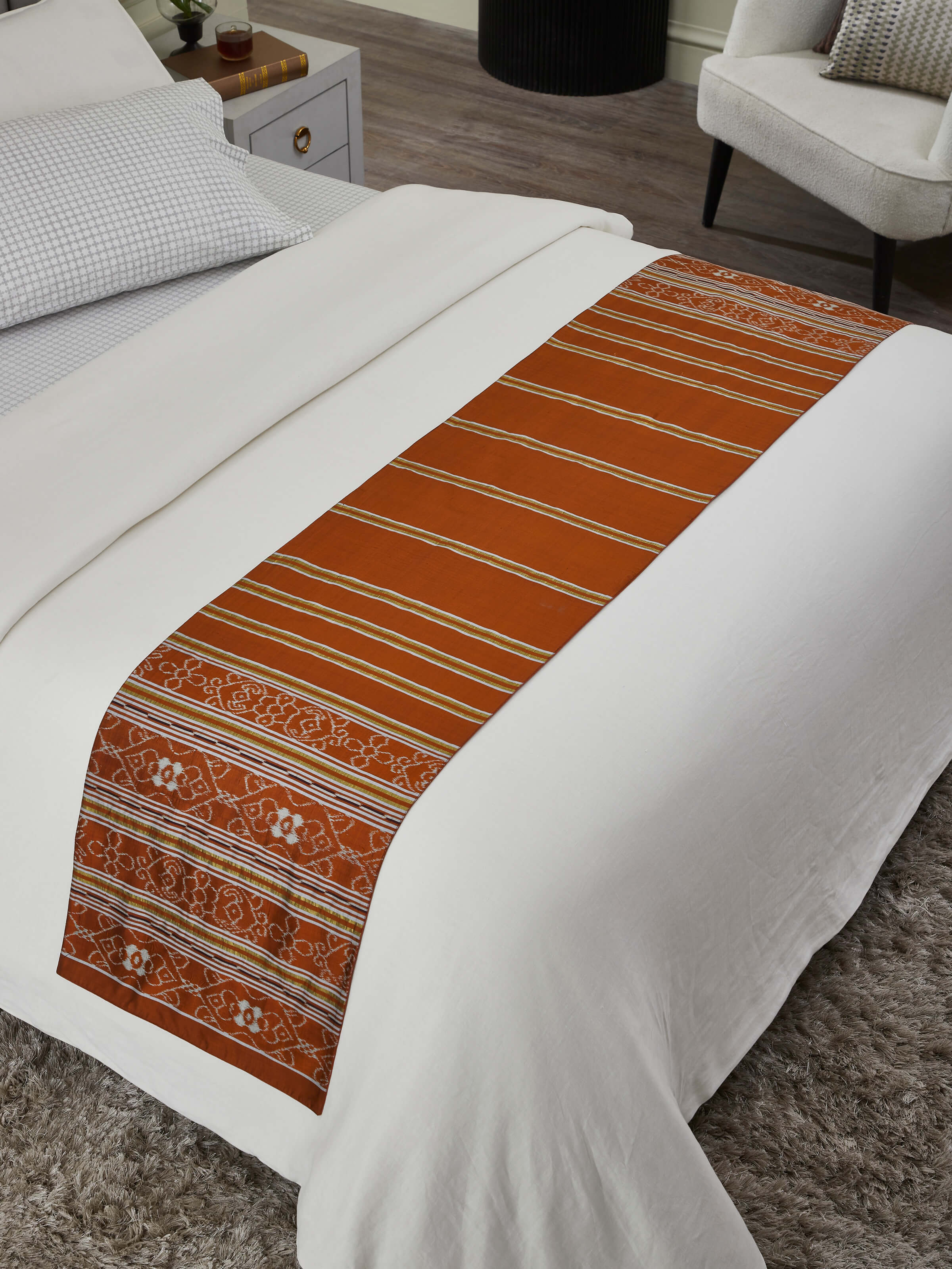 Lifestyle setting with rust striped bed runner placed across a neutral bedspread.