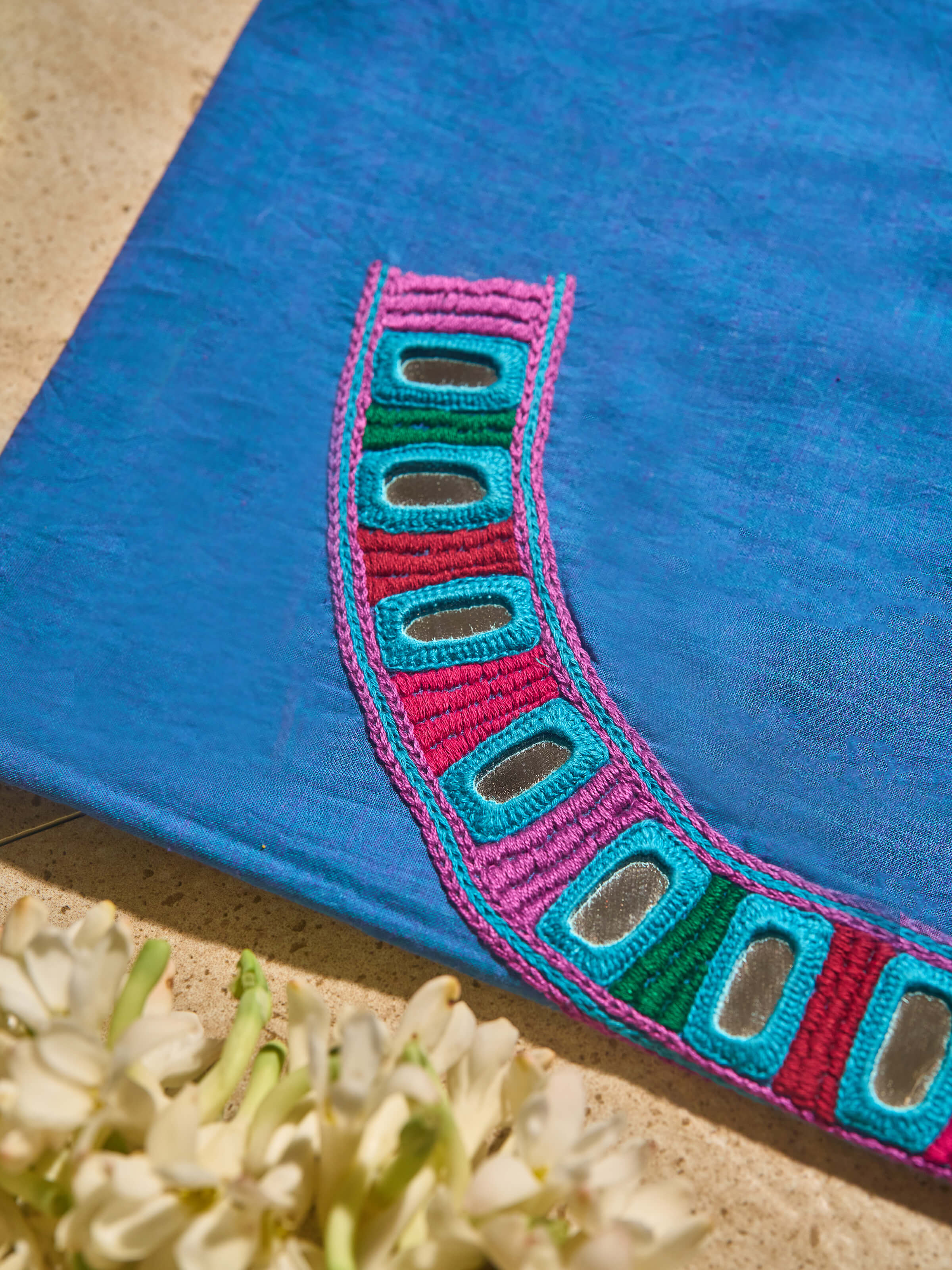 Close-up detail of hand-embroidered Lambani motifs on solid blue cotton blouse fabric