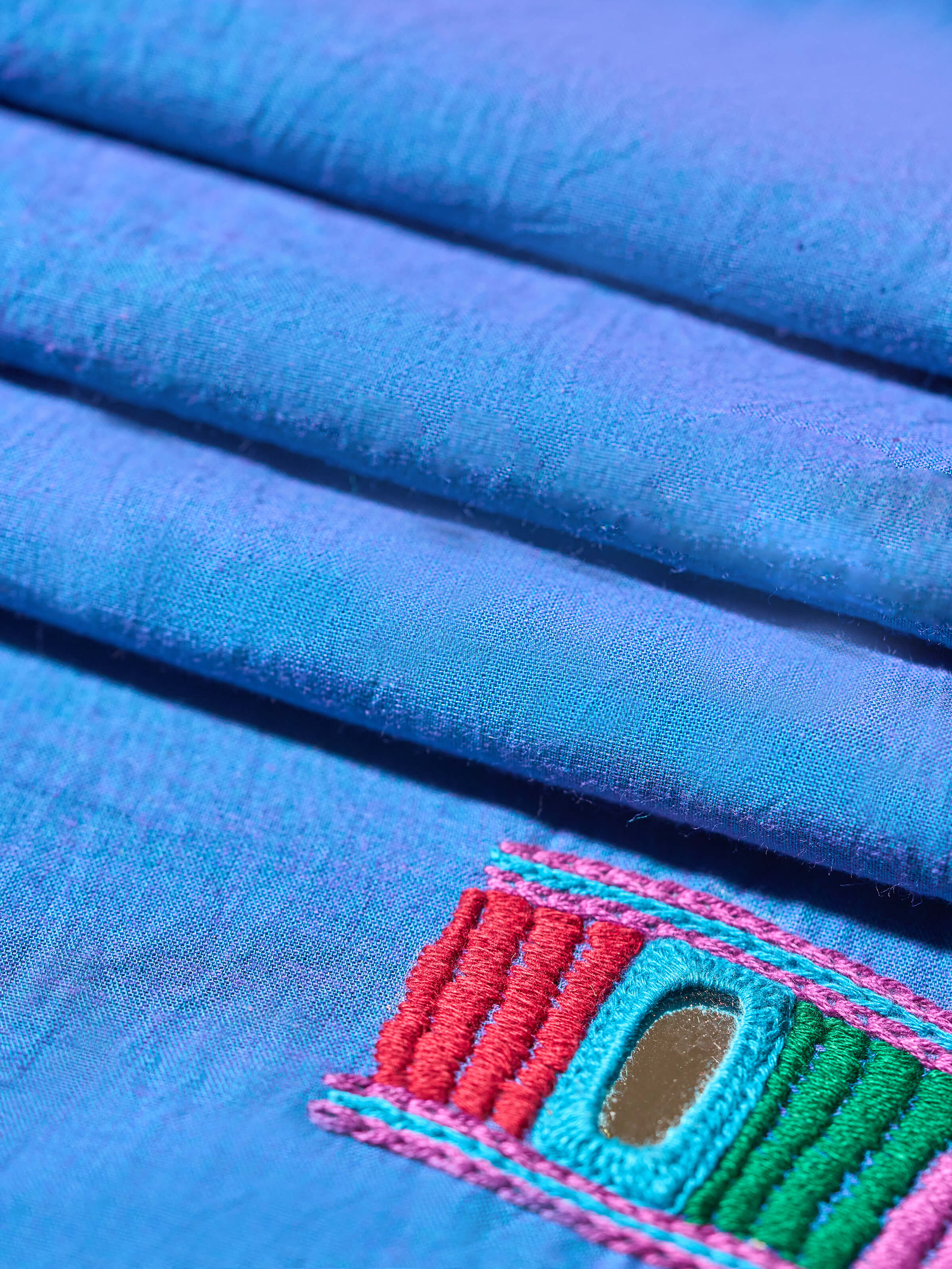 Back view of solid blue cotton blouse piece featuring traditional Lambani embroidery patterns