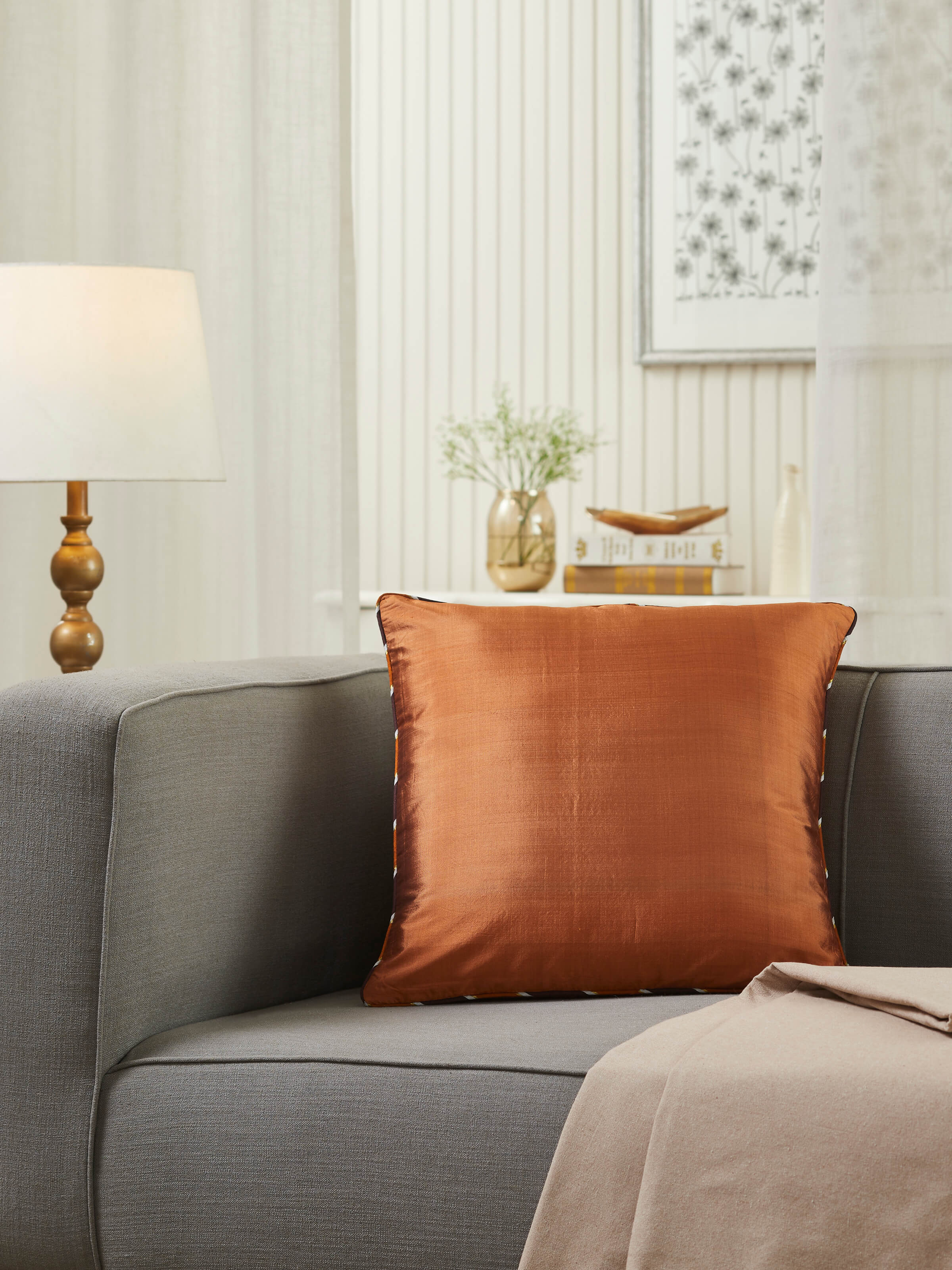 Lifestyle shot: Rust silk handloom cushion cover styled on neutral-toned seating for a warm accent.