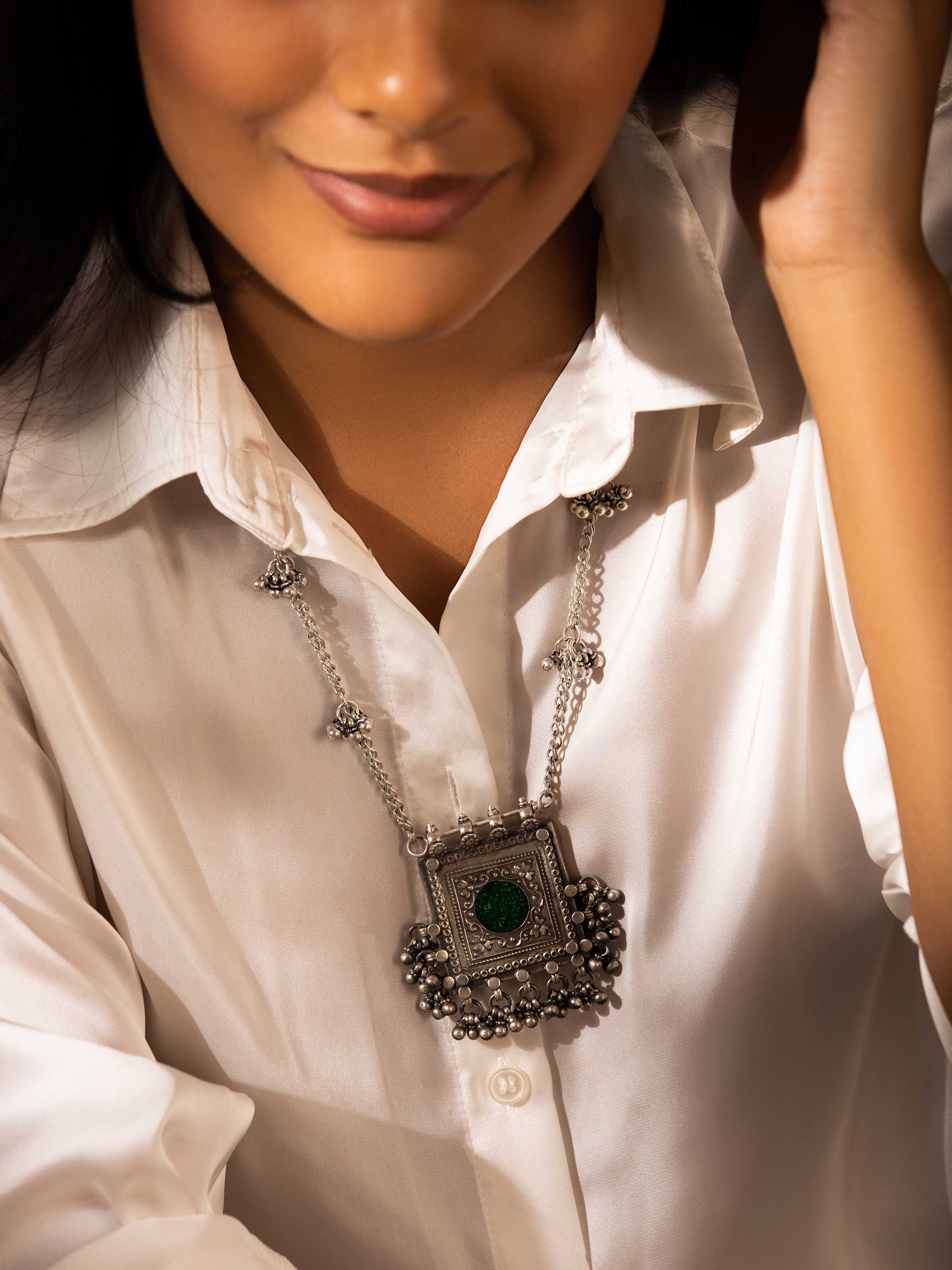 Close-up view of a silver smithing long necklace featuring an intricately crafted pendant with detailed patterns, suspended from a delicate silver chain.