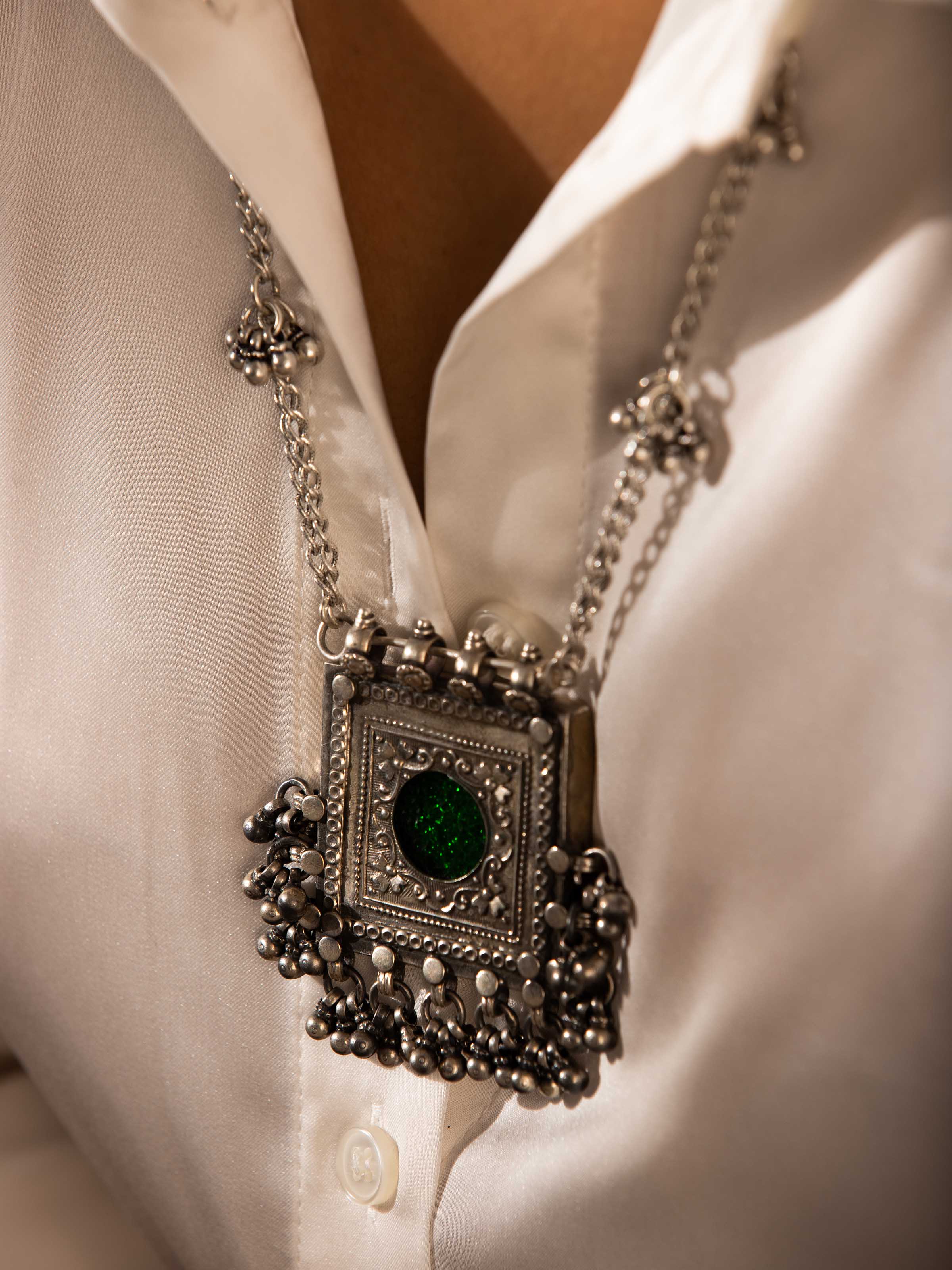 Side Close-up view of a silver smithing long necklace featuring an ornate circular pendant with fine detailing.