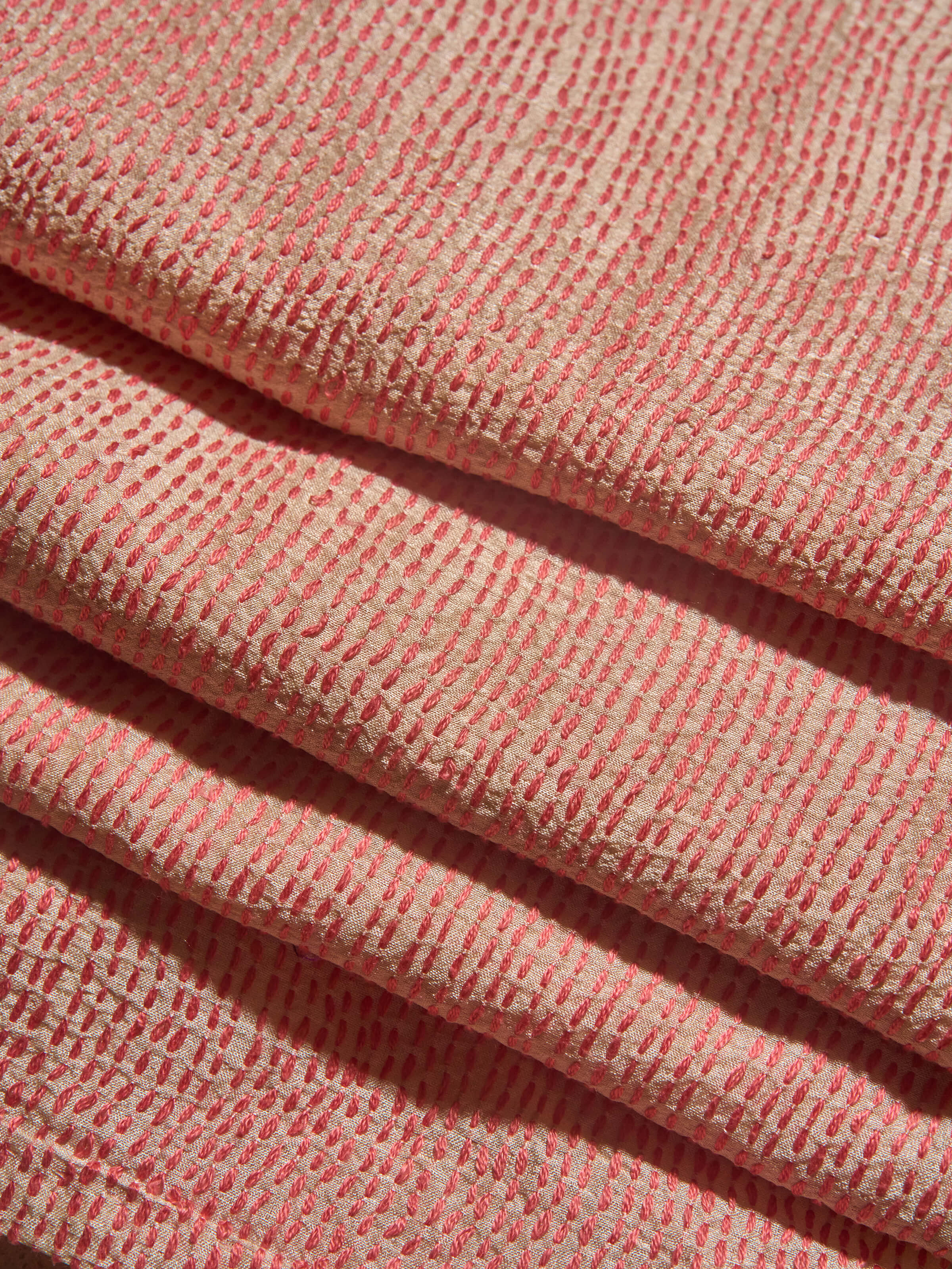 Off-white tussar silk blouse fabric laid flat showing colorful Sujani embroidery motifs.