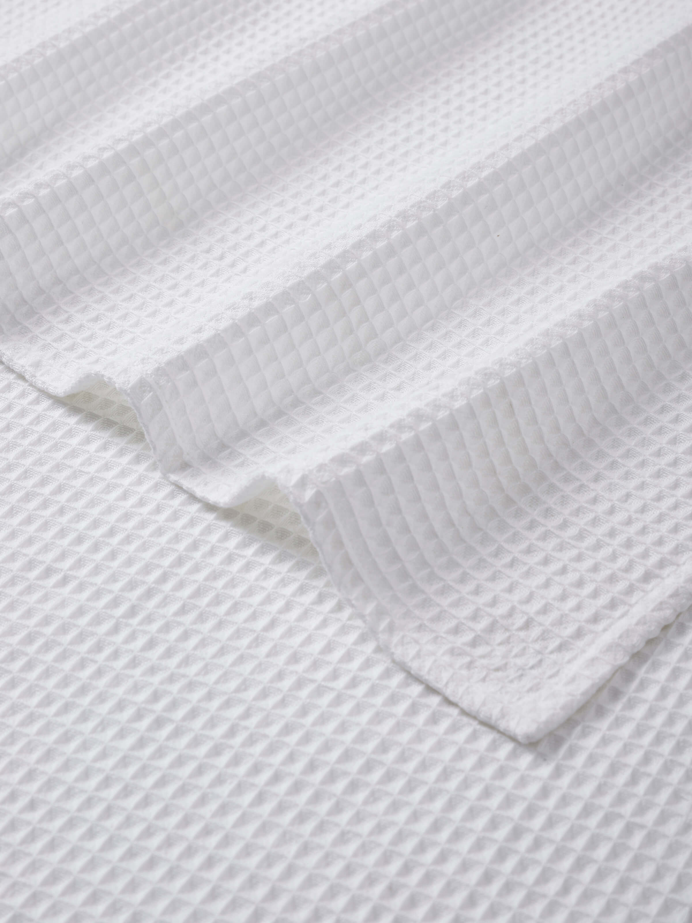 Angled view of Amala waffle white solid cotton bath towel (M), illustrating the towel's full size and waffle knit detail