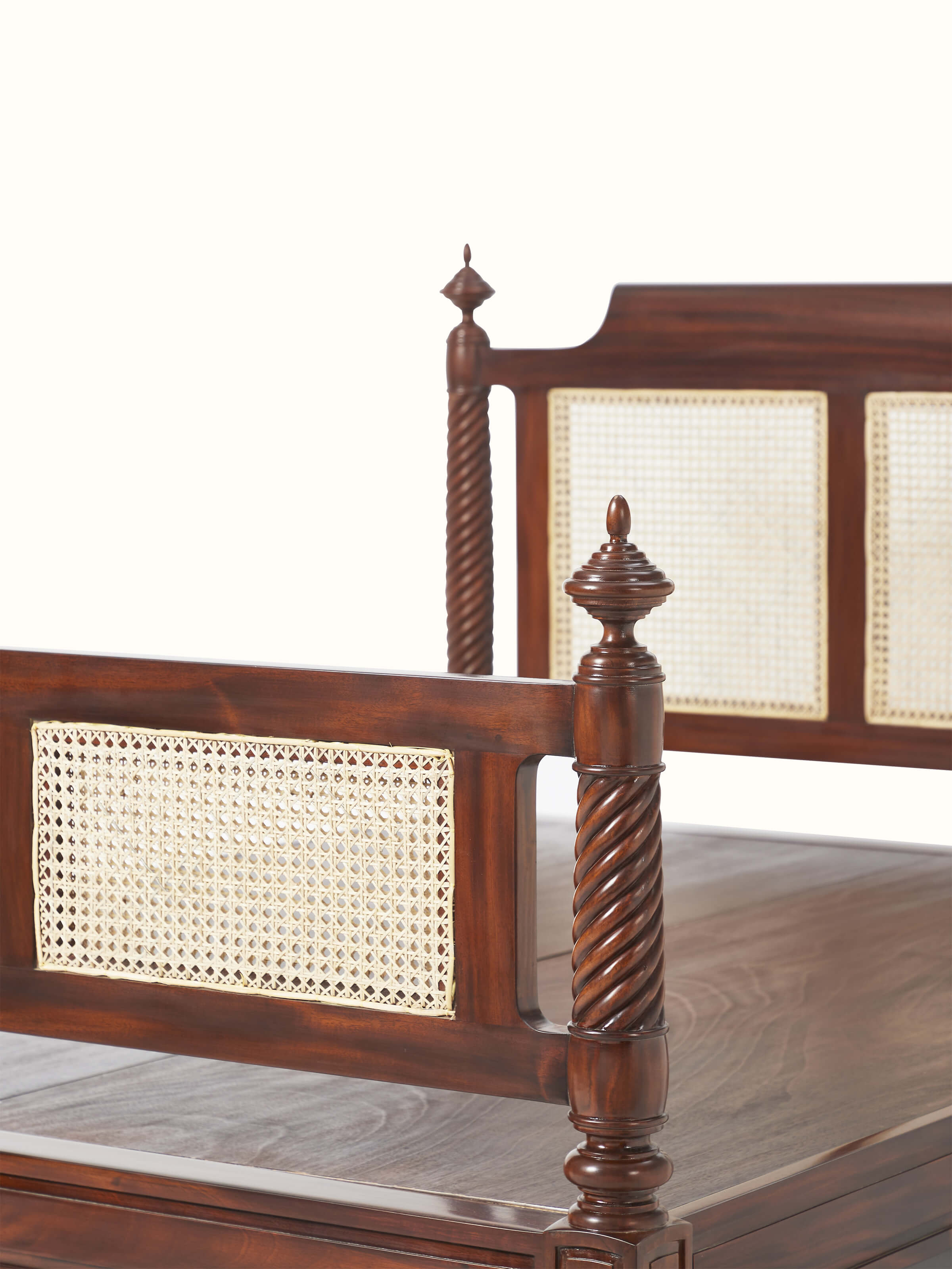 Angle view of the carved mahogany wood queen bed with cane detailing, showing the bed's depth and decorative features.