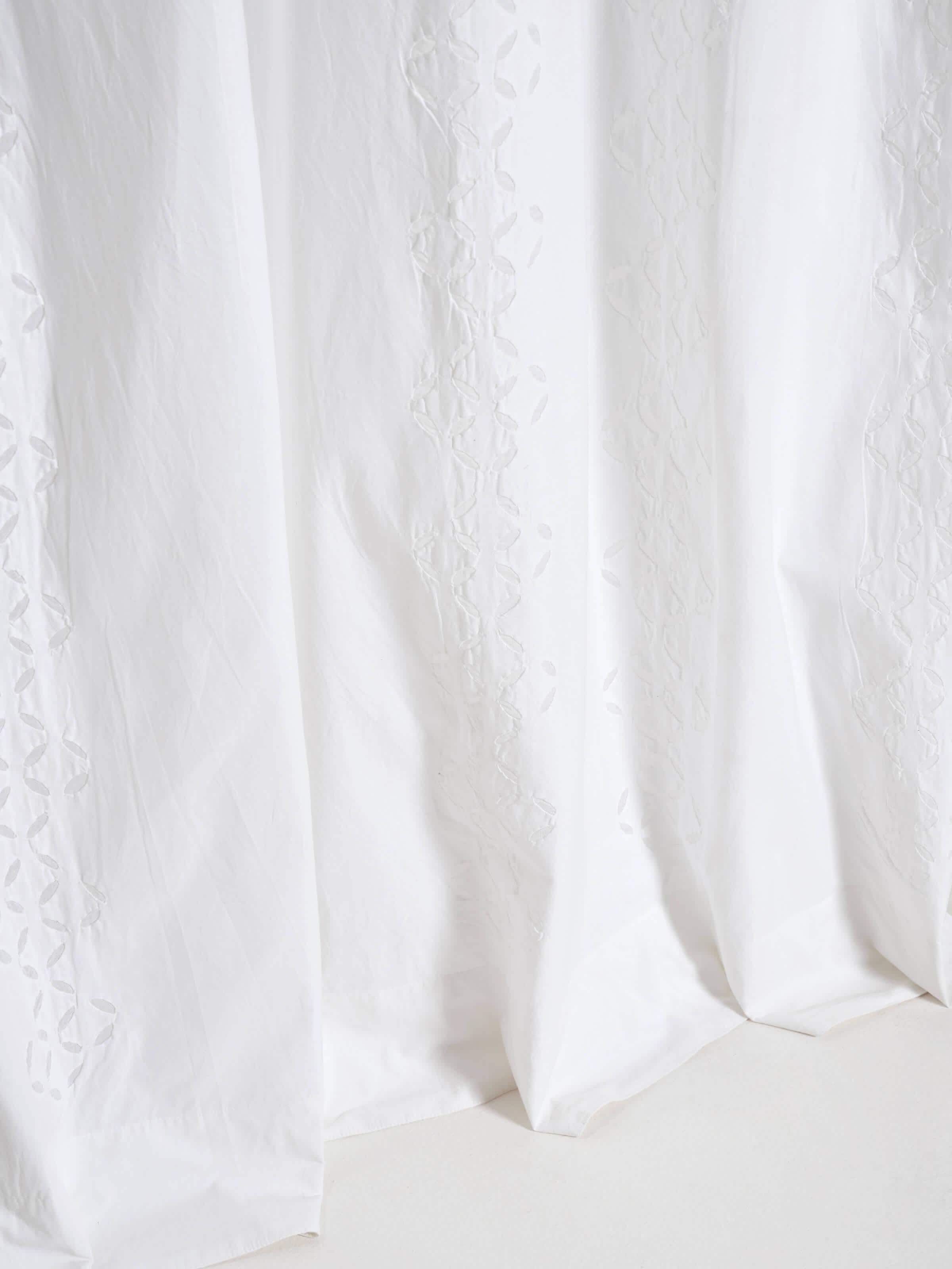 Mandana white cotton sheer curtain with trellis stripes and applique design, draped gracefully to showcase its texture.