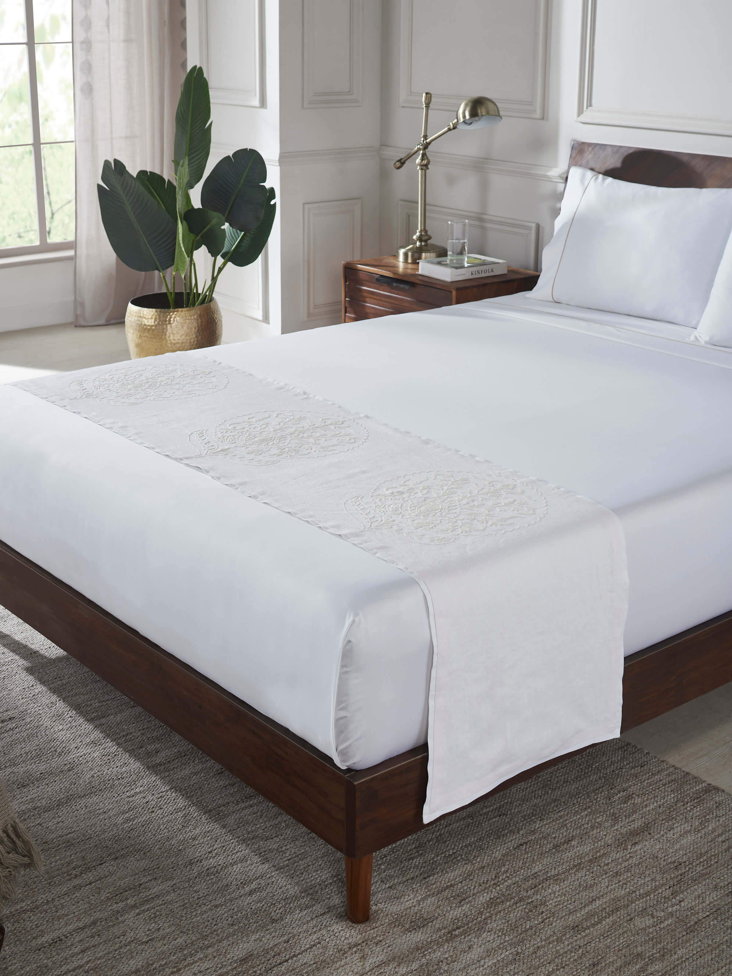 Lifestyle view of white crewel-embroidered linen bed runner with floral buta design.