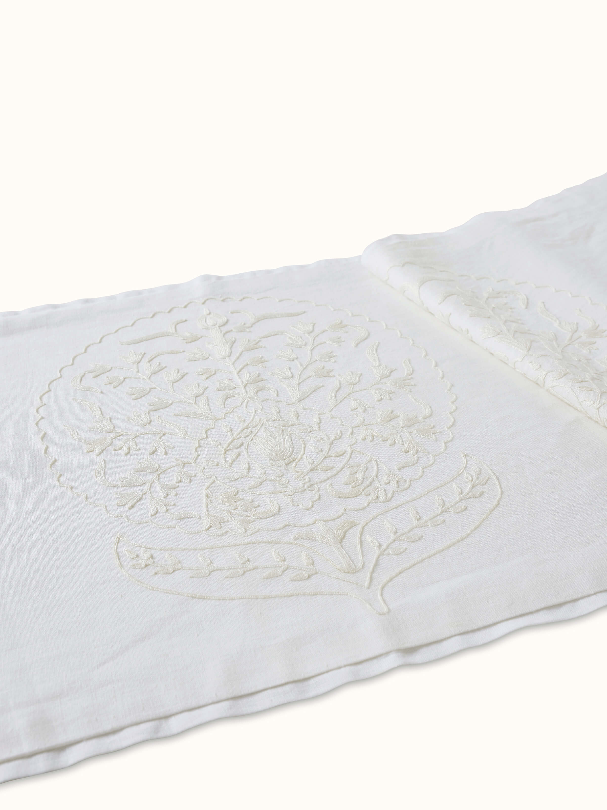 Detail shot showing intricate crewel work and floral motifs on white linen bed runner.