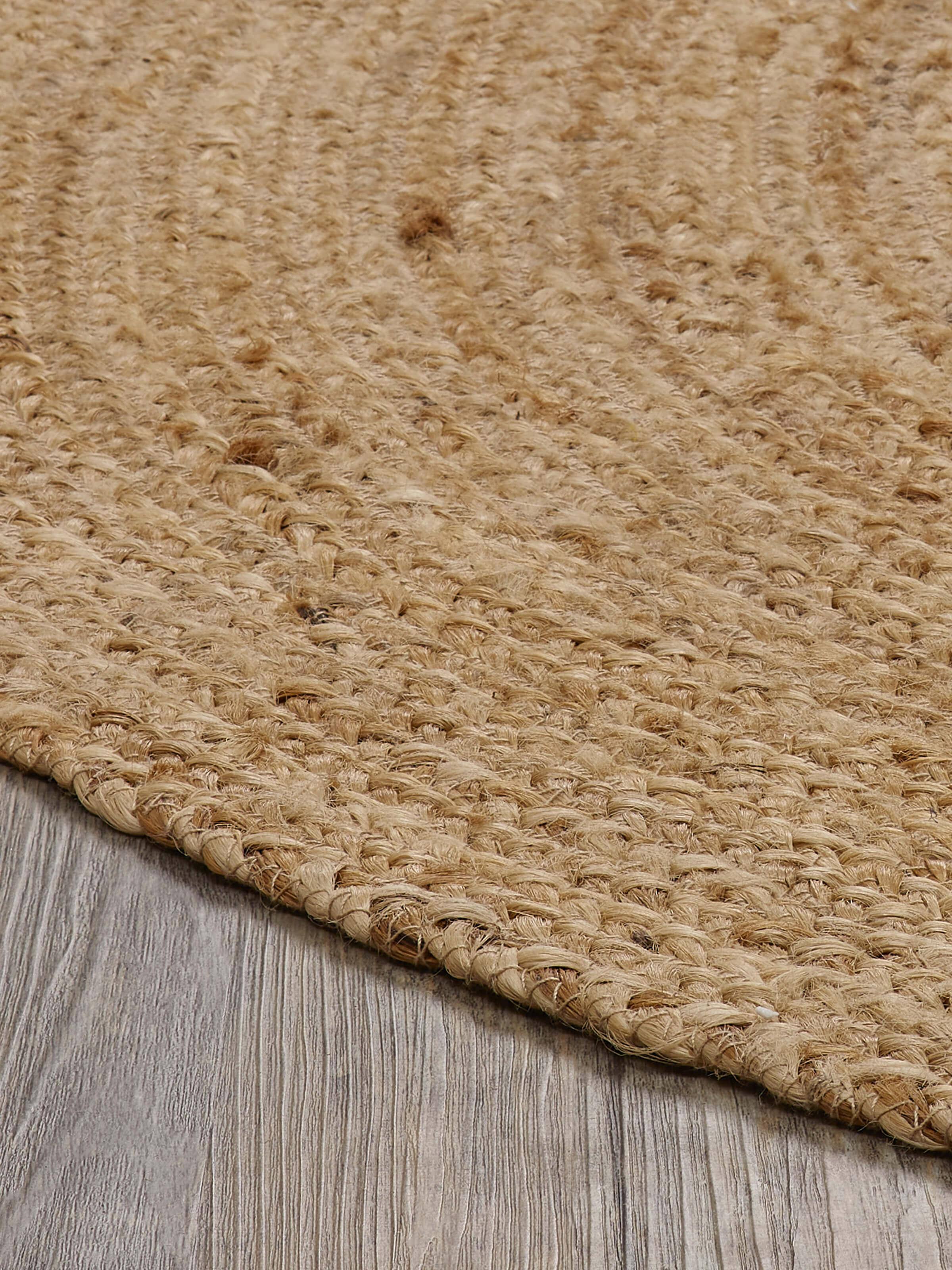 Braided round beige jute natural fibre rug, laid out to display its full round shape and texture.