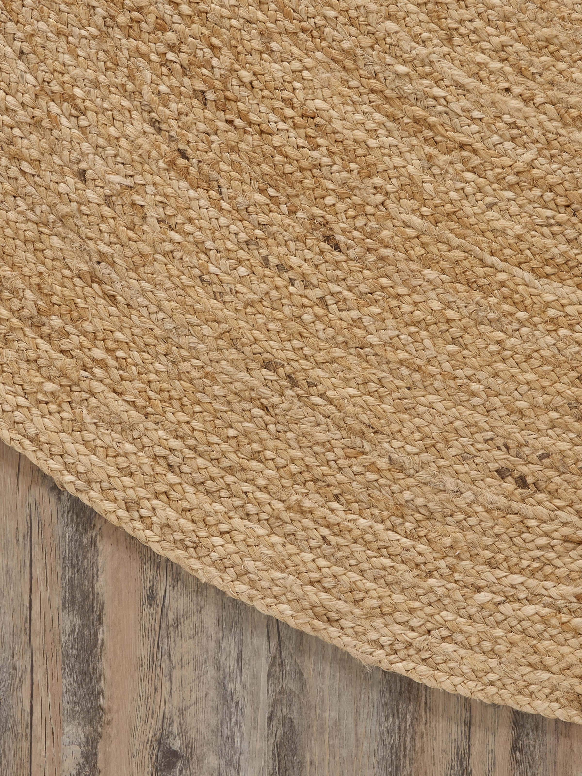 Braided round beige jute natural fibre rug, showing its placement in a room setting.