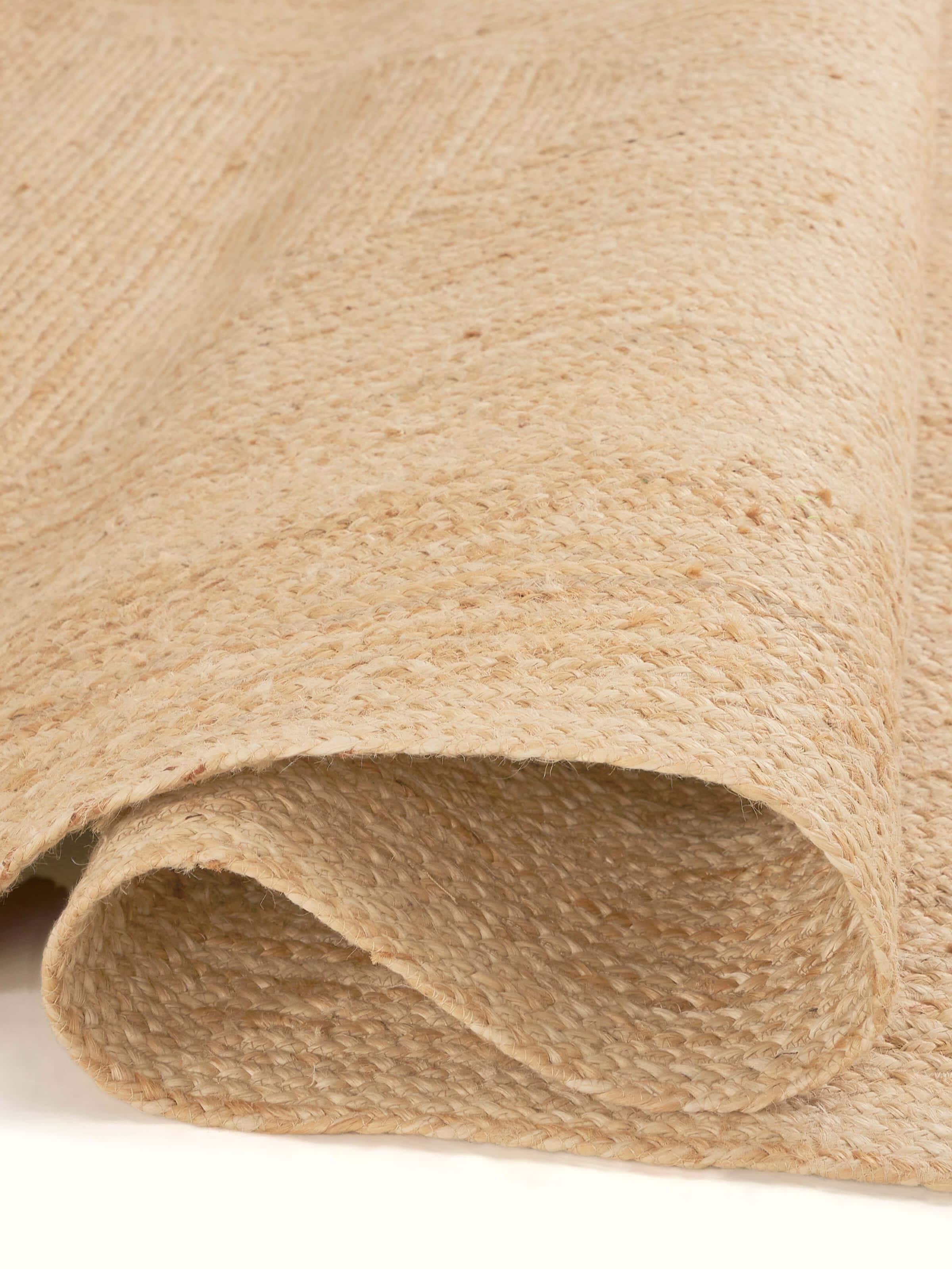 Side view of braided concentric rectangle beige Lawan jute rug, emphasizing its layered braided structure and natural color