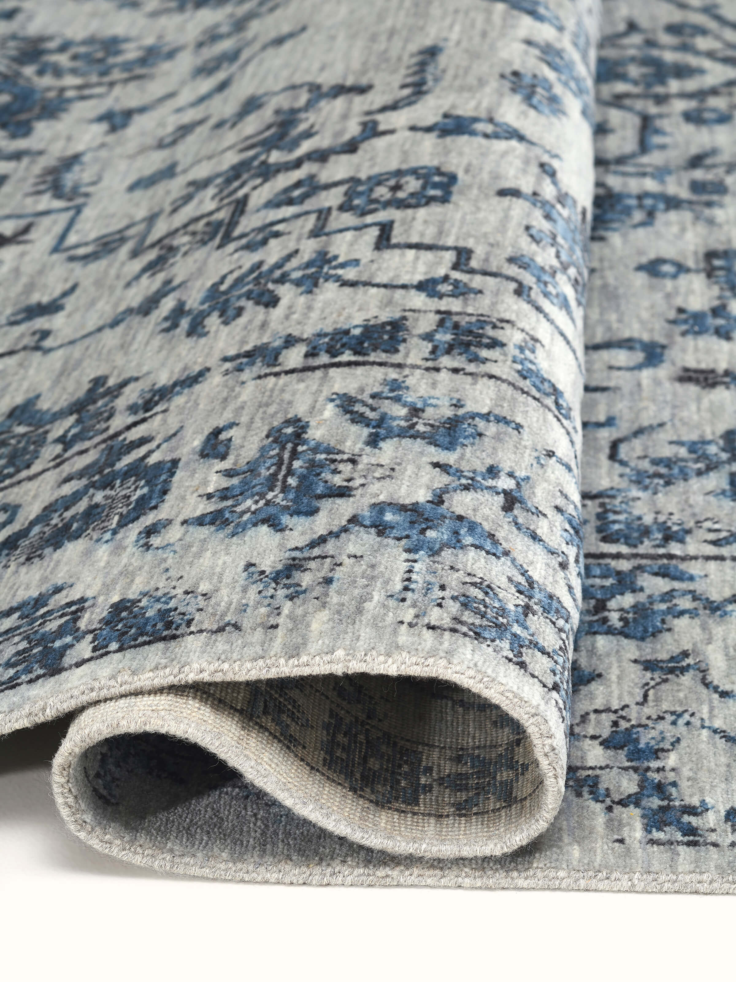 Side perspective showcasing the handcrafted edges of the Transitional Grey Blue Agra Wool Rug by Swadesh.