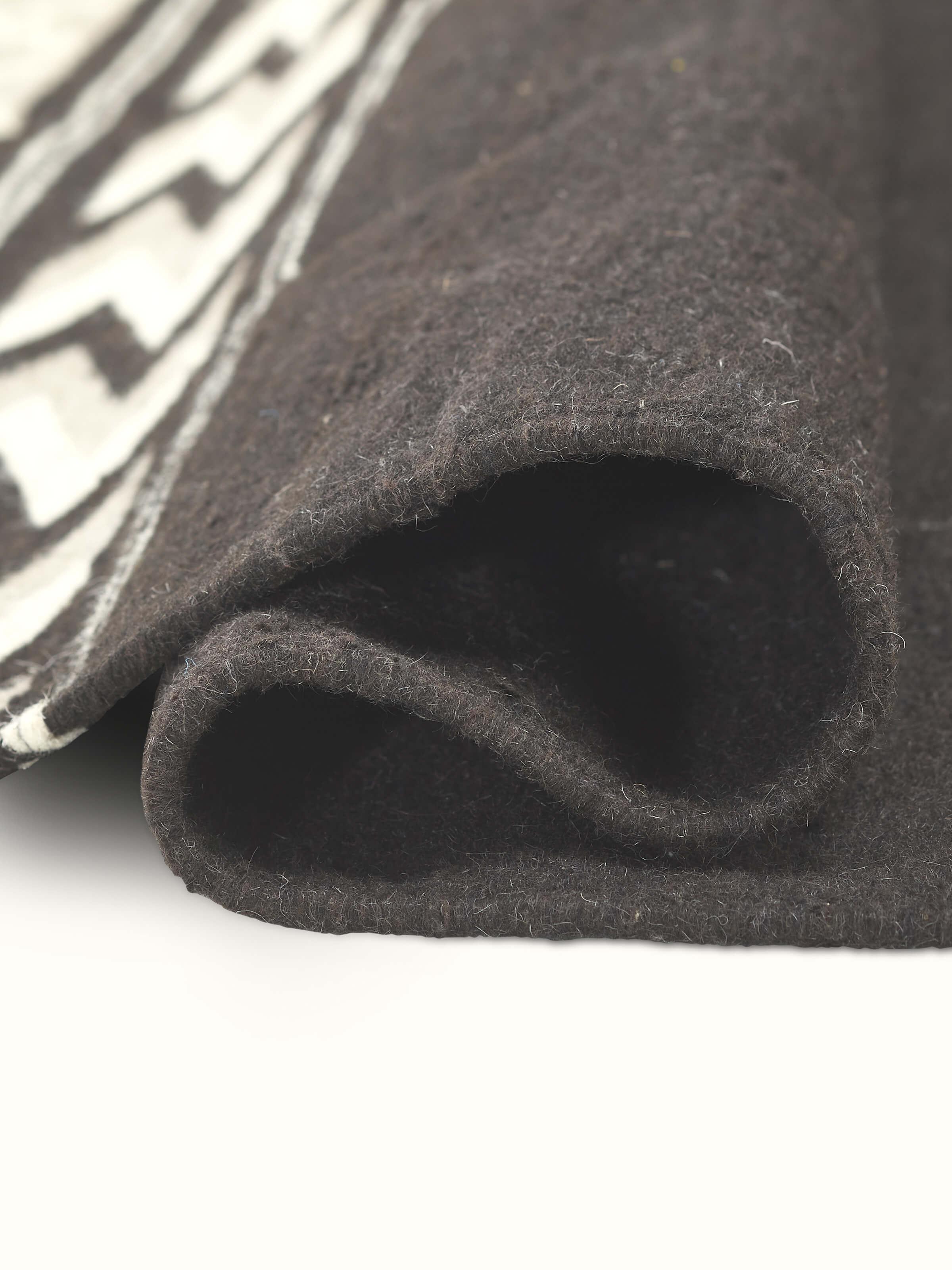 Side view of Geo border dark brown Gujarat wool & cotton panja dhurrie kharad (3x5 ft) showing the thickness and design