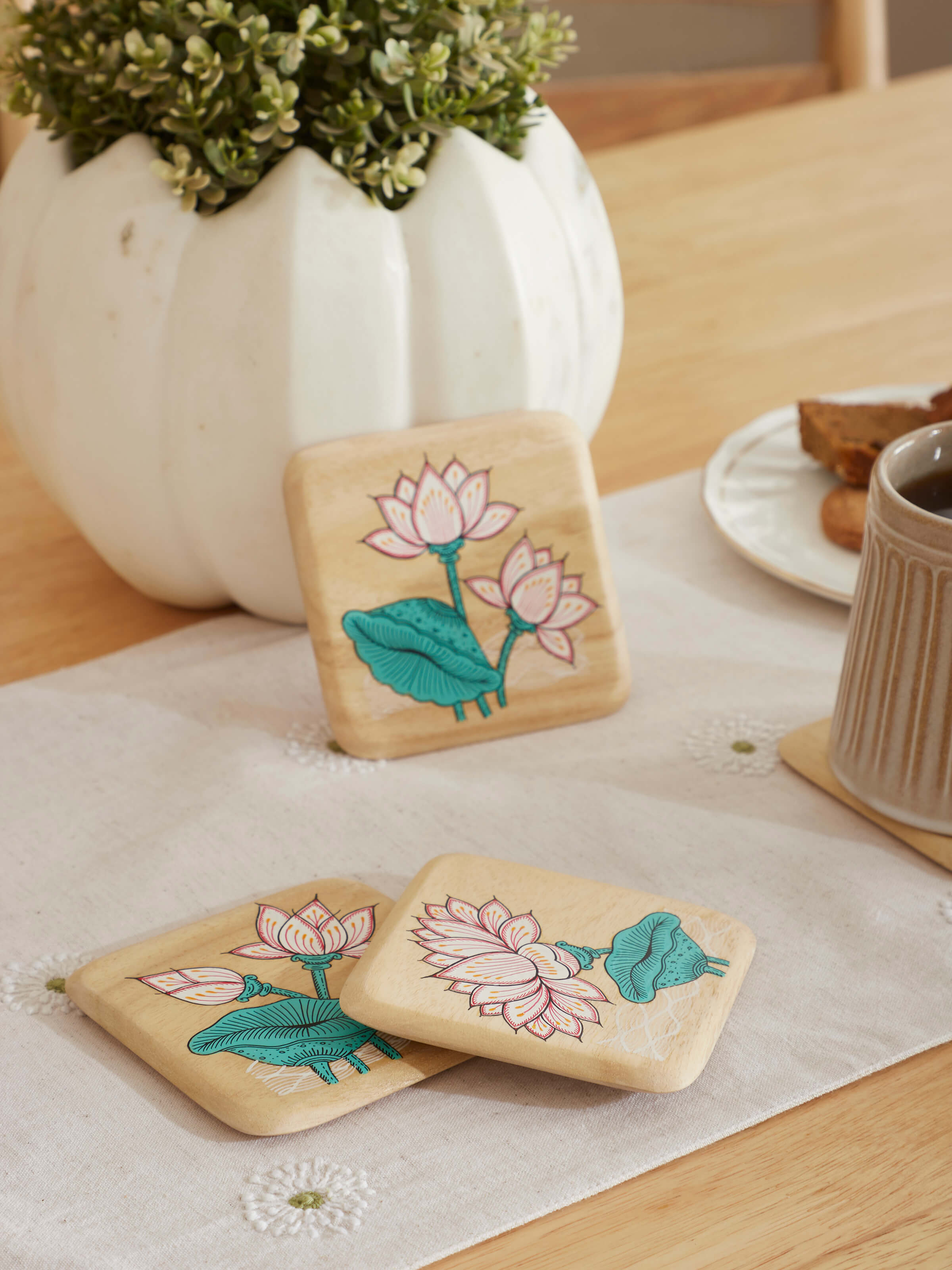 Close-up view of the carved gamhar wood coasters in white and teal, showcasing the detailed carvings and color contrast.