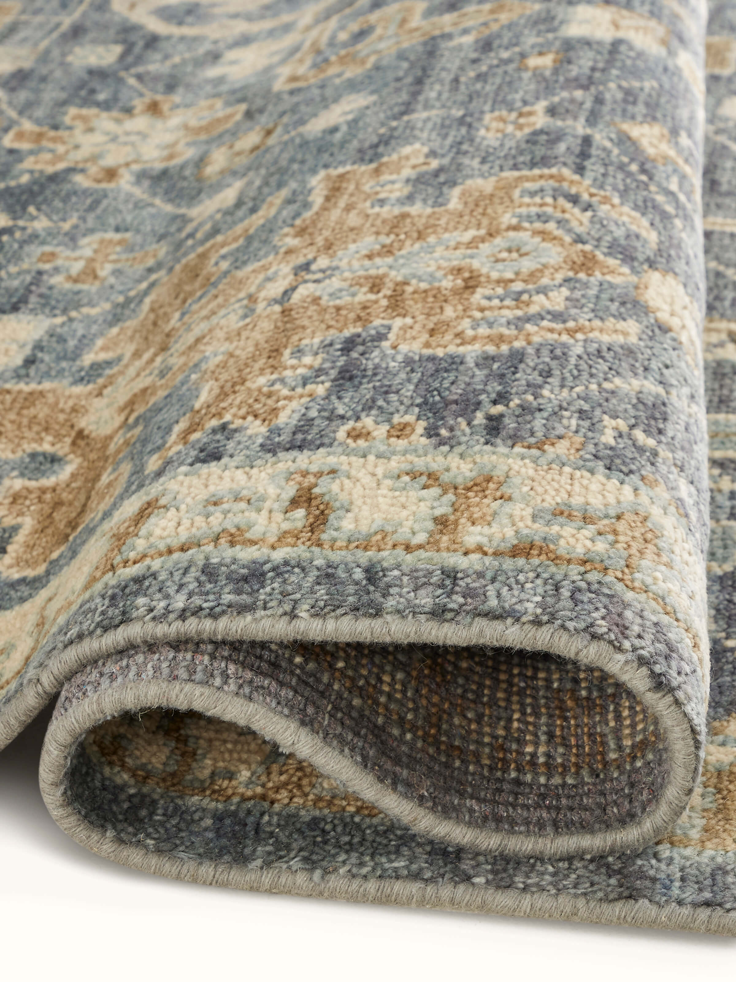 Angled view of Oushak traditional blue Bhadohi wool hand-knotted rug kharad showing the full pattern and edge detailing.