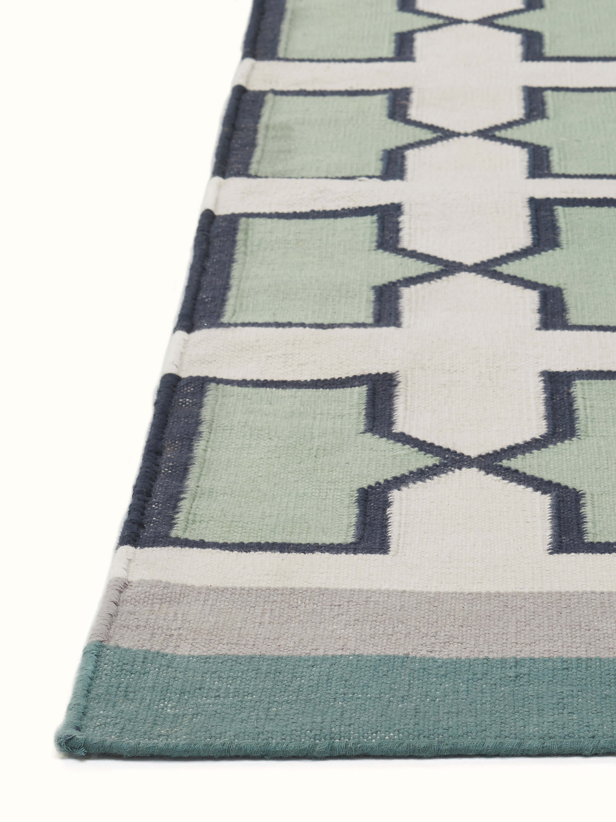 Angled view of Modern Geo Jharokha green grey Lawan cotton Panja dhurrie, illustrating its pattern and fabric drape