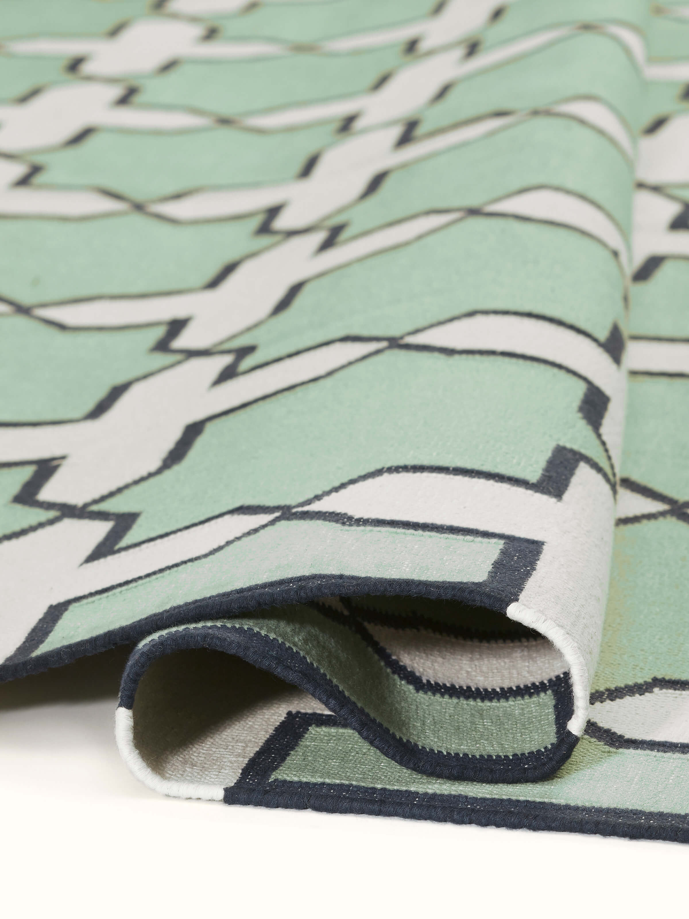 Side view of Modern Geo Jharokha green grey Lawan cotton Panja dhurrie, showing its thickness and border details