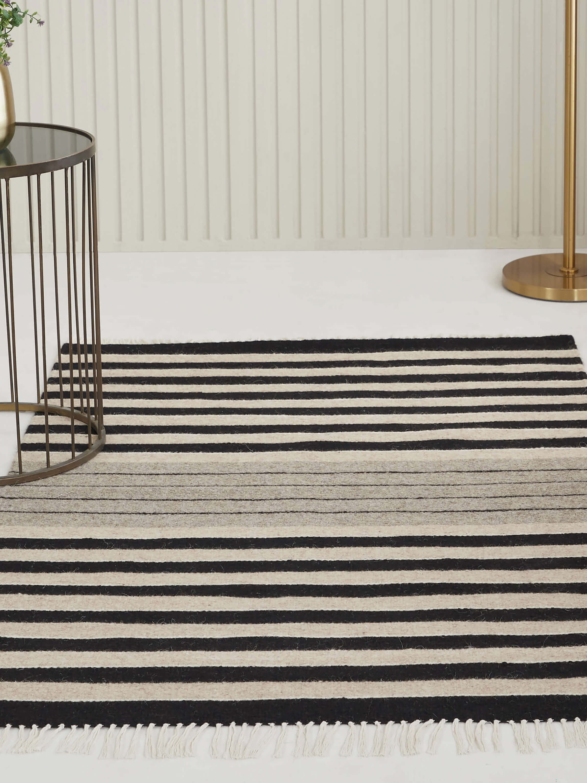 Lifestyle view of Jawaja wool dhurrie in black and beige stripes styled in a rustic setting