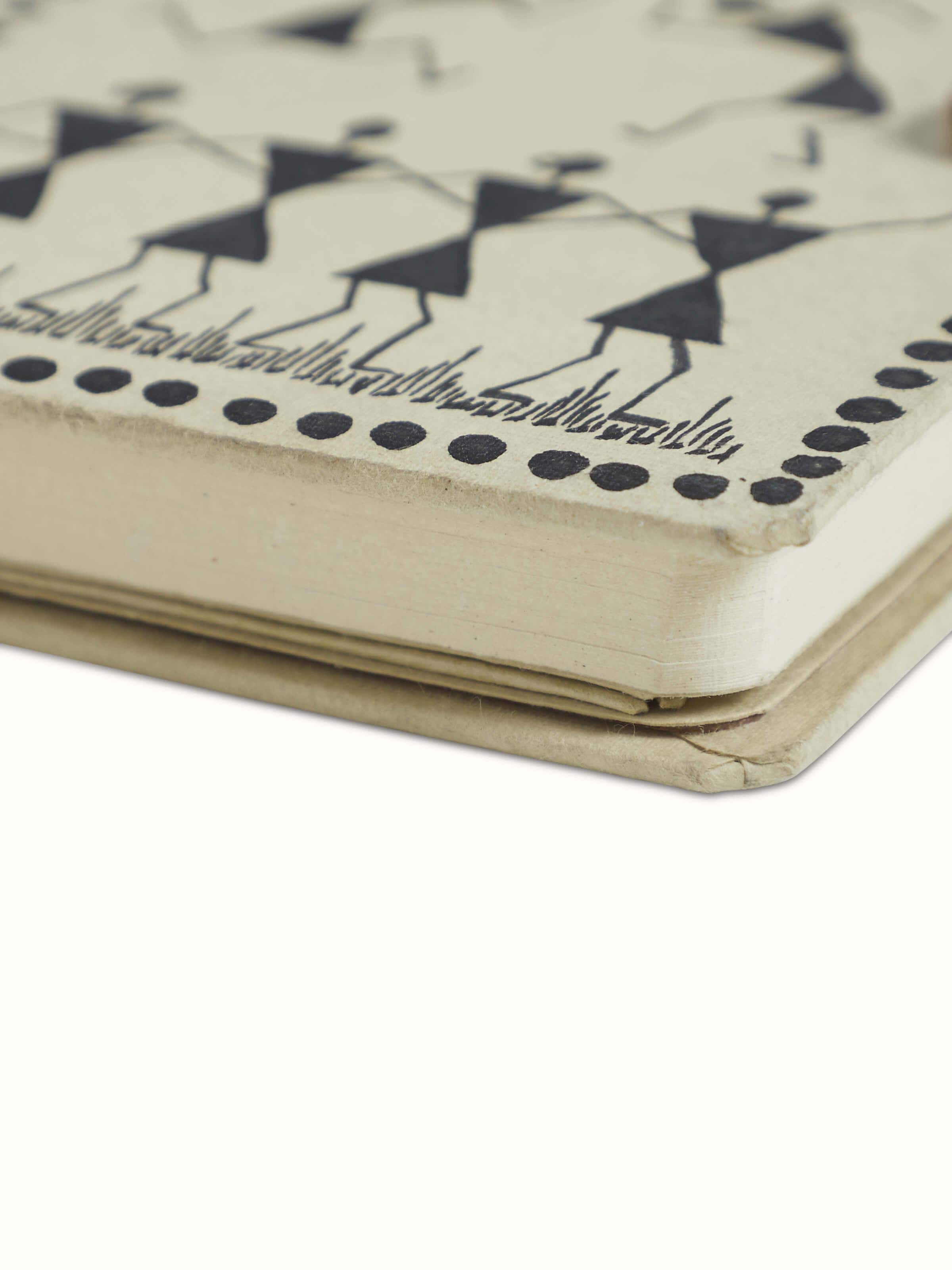 Open view of Warli painted paper journal in brown showing the inner pages and traditional artwork on the cover