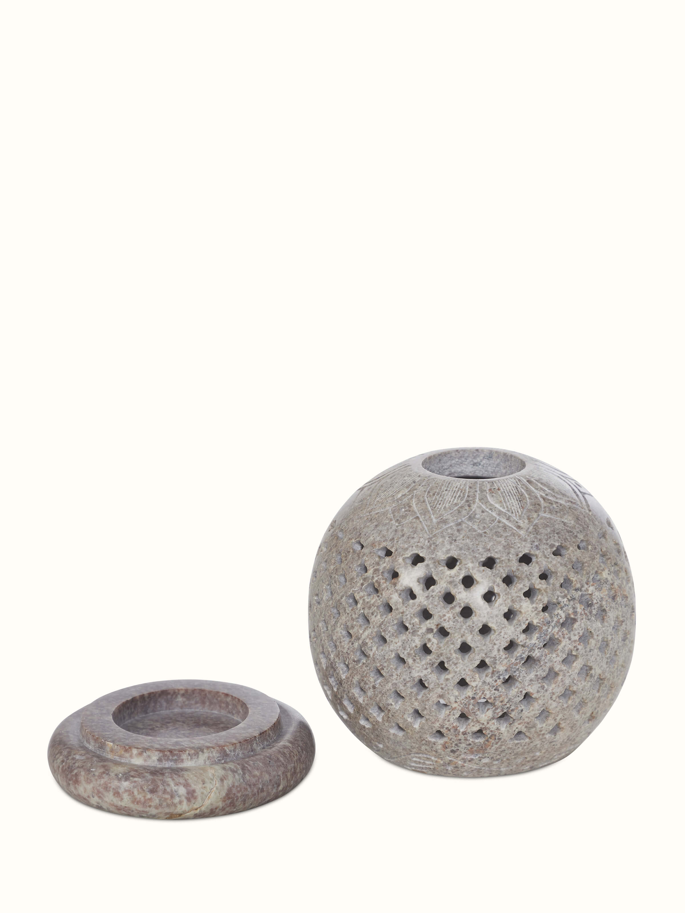 Angle view of carved stone tea light holder, showcasing the elegant carvings and shadow play